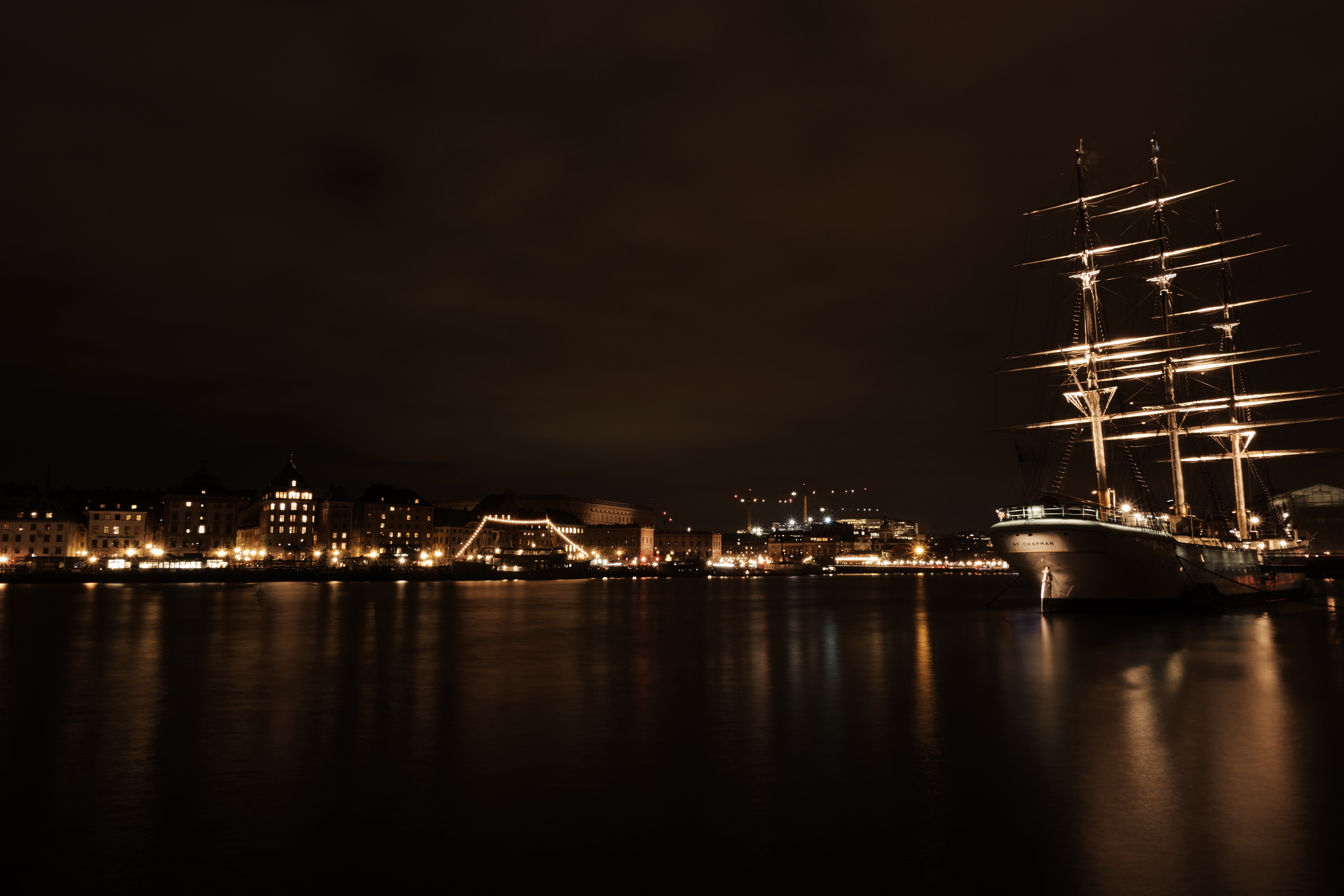 Tall ship docked at night with illuminated cityscape reflection HD Wallpaper