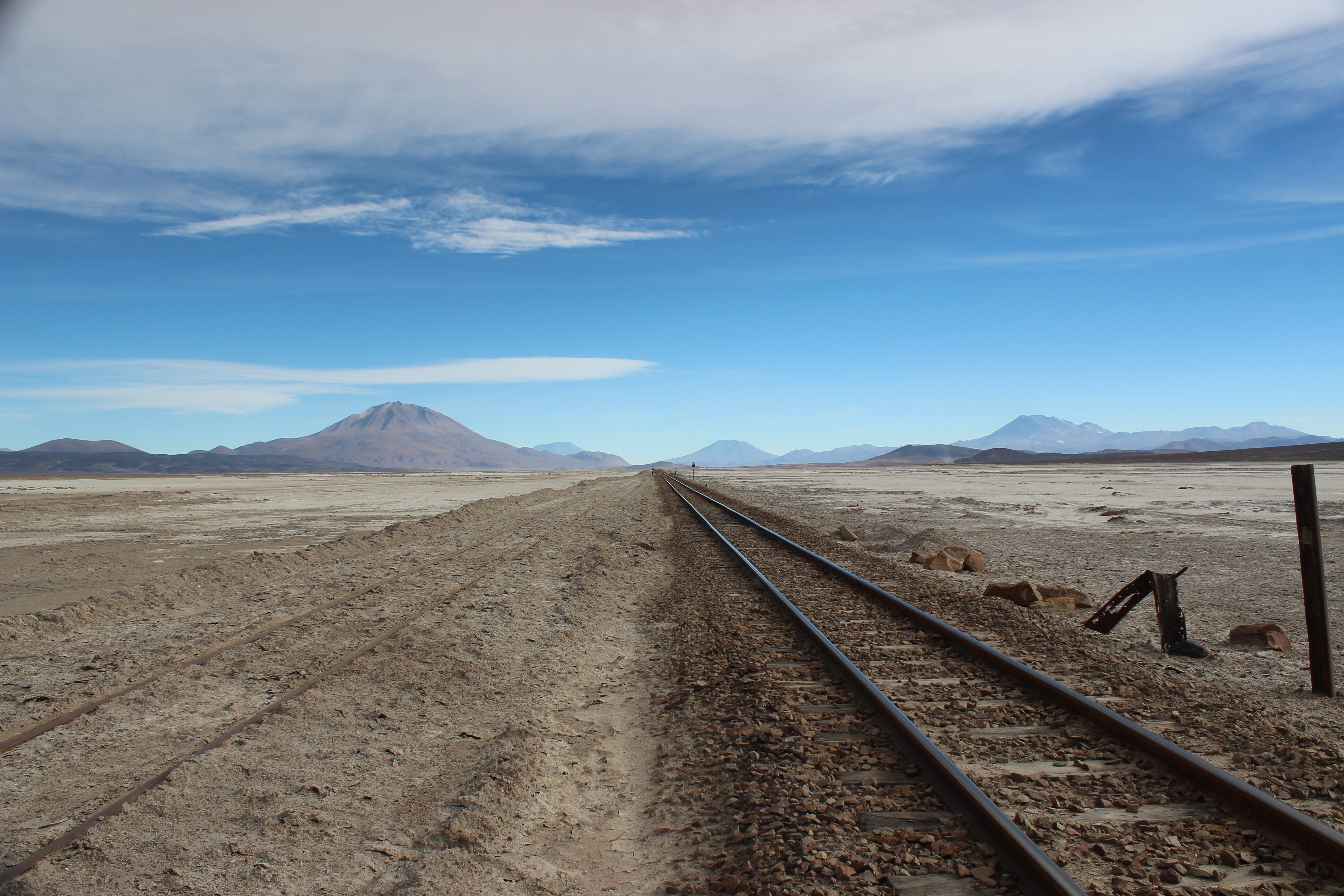 Railway tracks in a vast, arid landscape with mountains under a blue sky HD Wallpaper