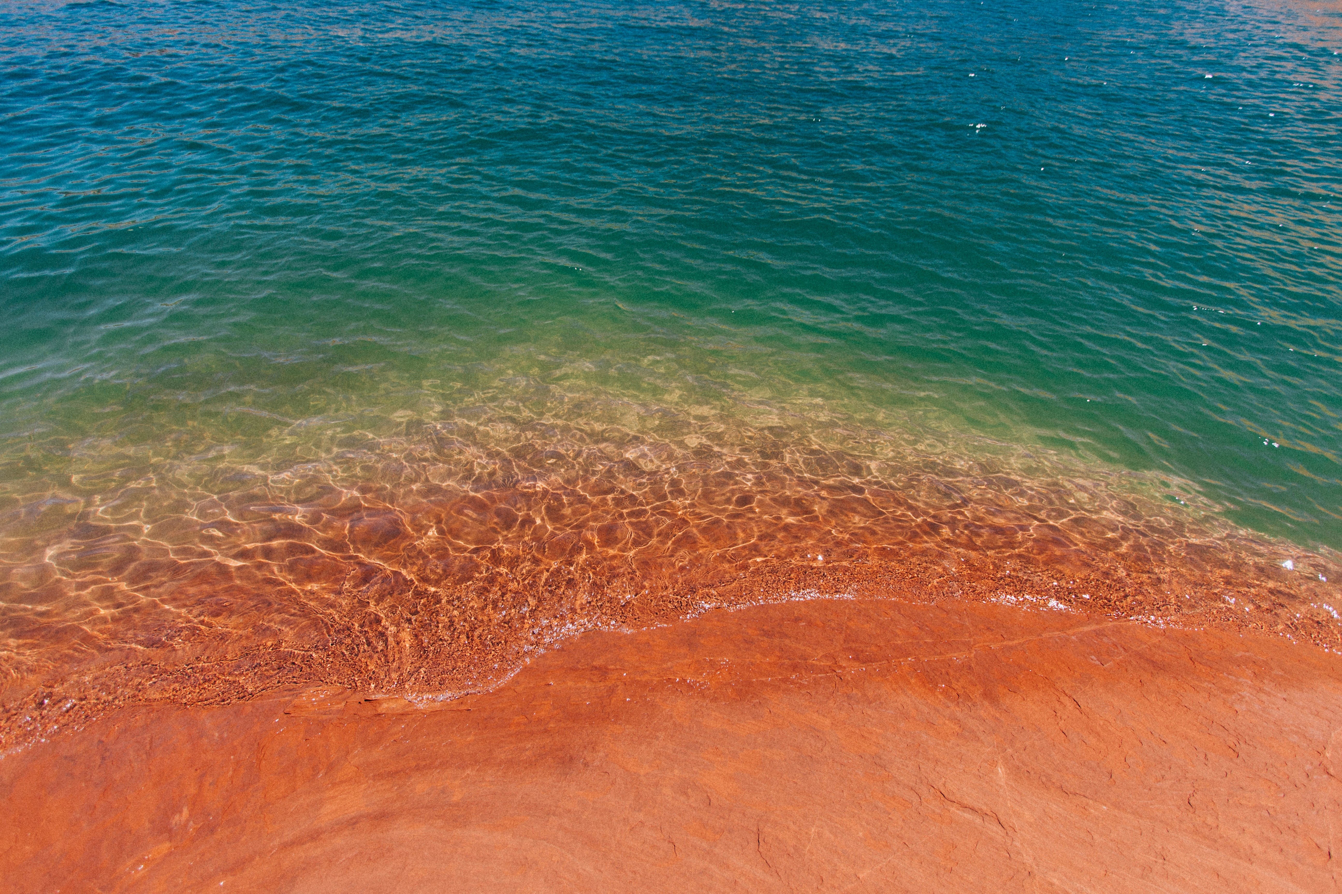 Turquoise water meets a red sandy shore HD Wallpaper