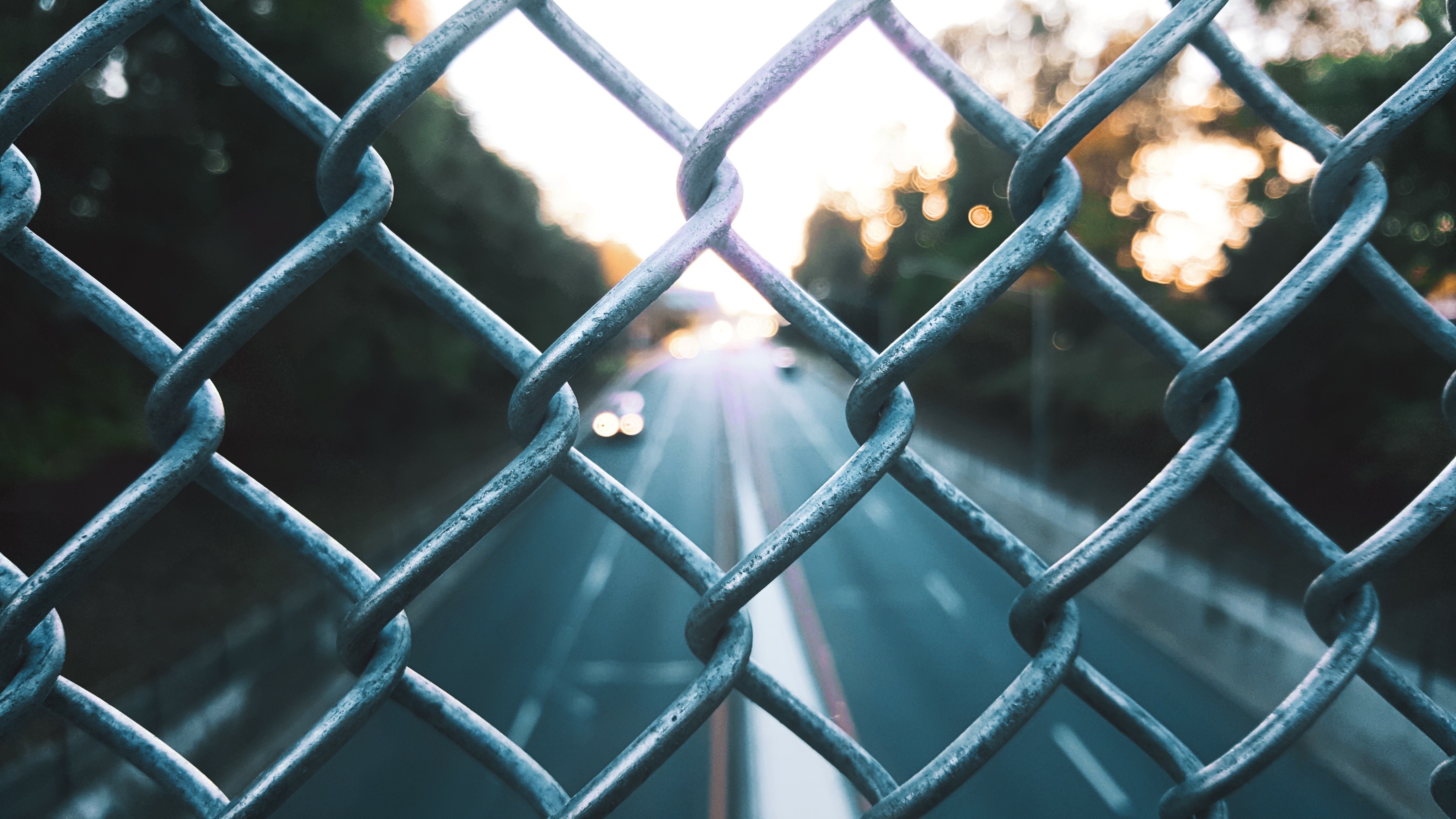 Chain-link fence in front of a highway at sunset HD Wallpaper