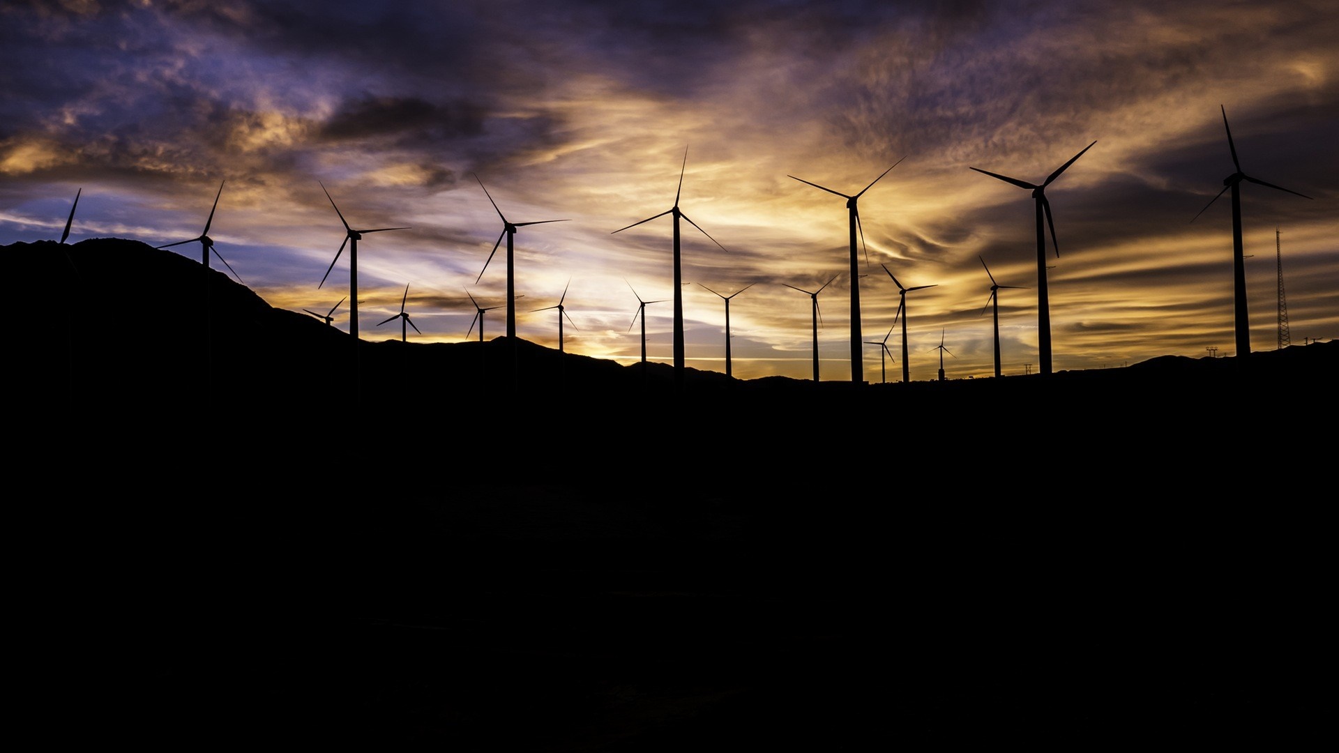 Wind turbines silhouetted against a dramatic sunset sky HD Wallpaper