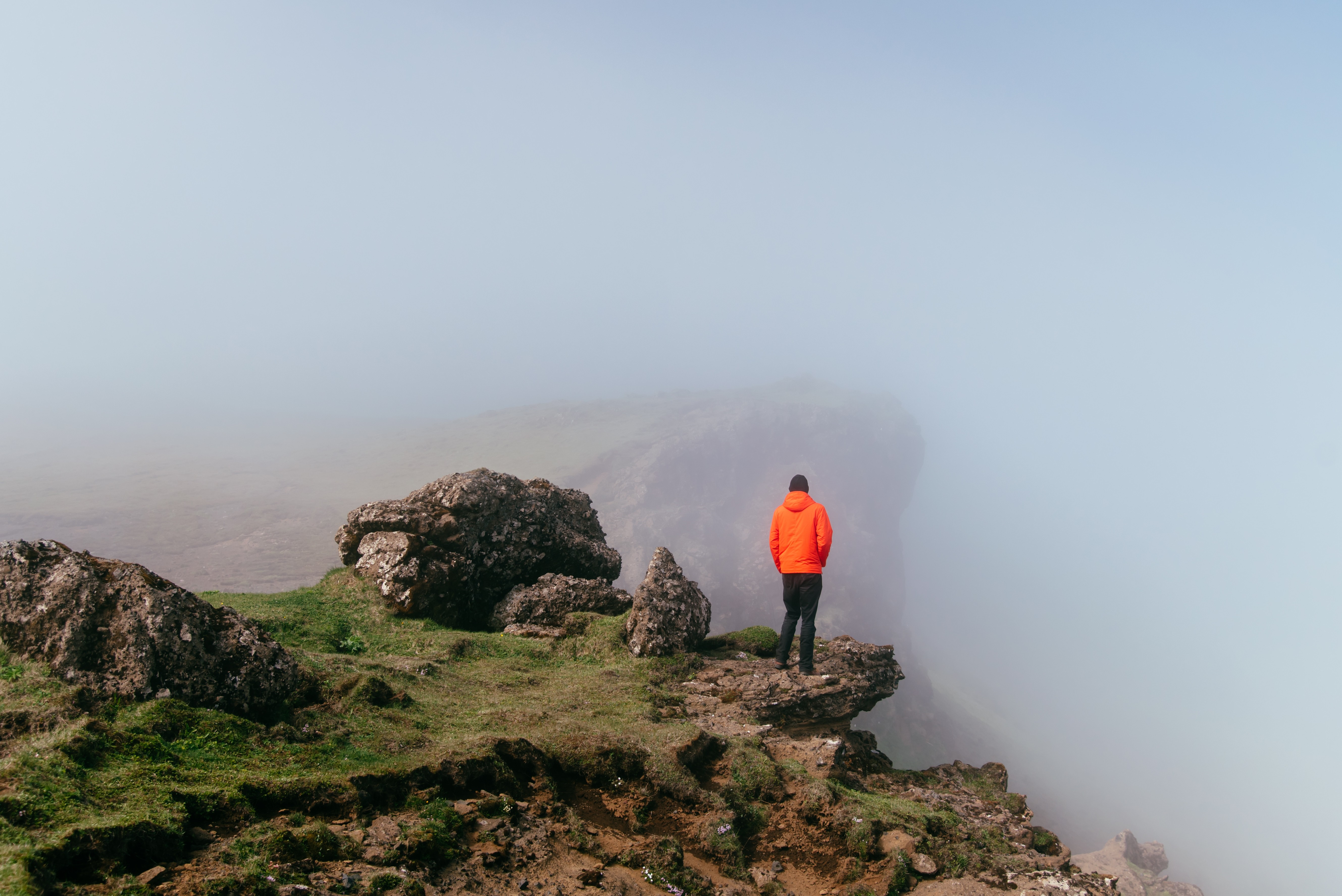 Man in orange jacket on foggy cliff edge HD Wallpaper