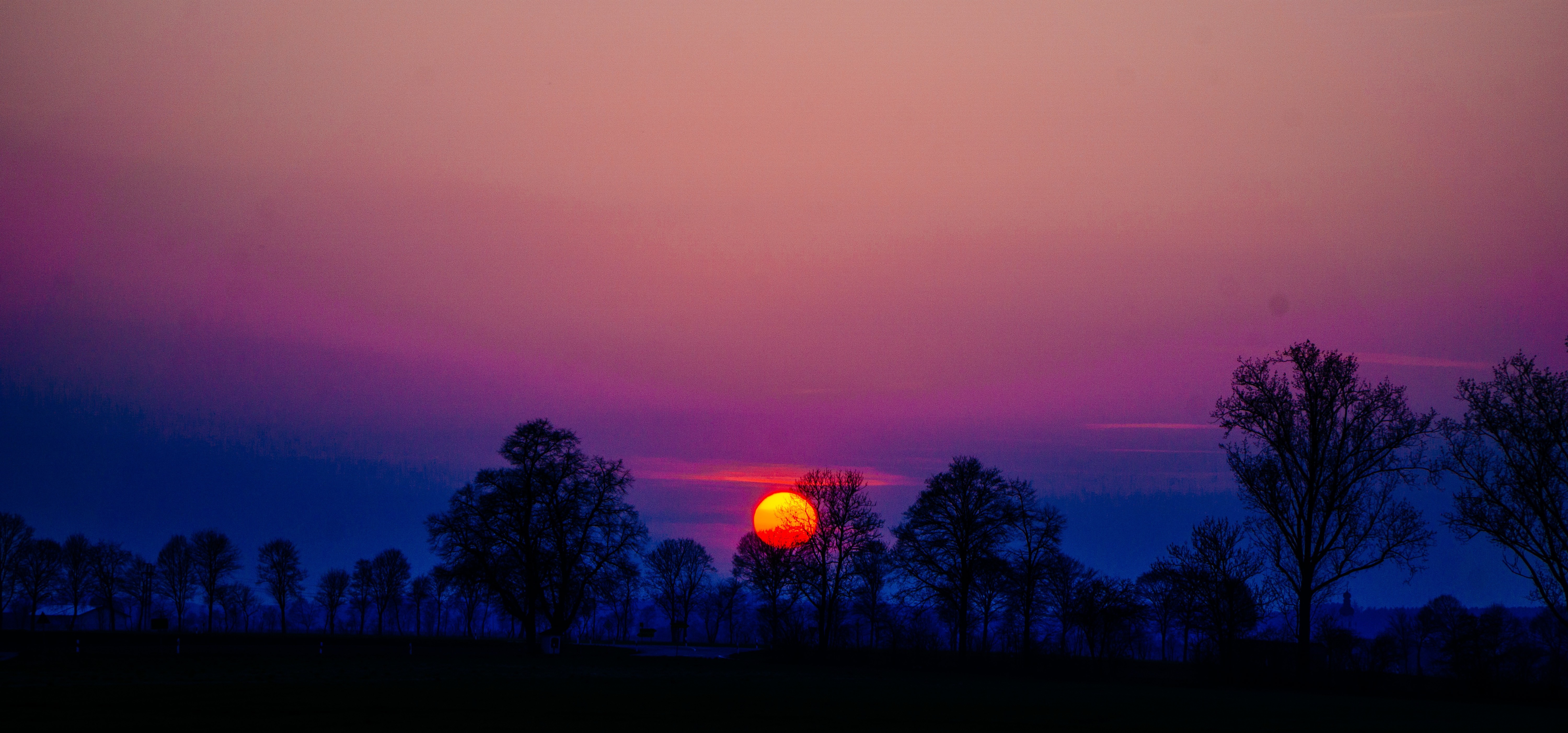 Sunset over a silhouetted treeline with vibrant sky HD Wallpaper