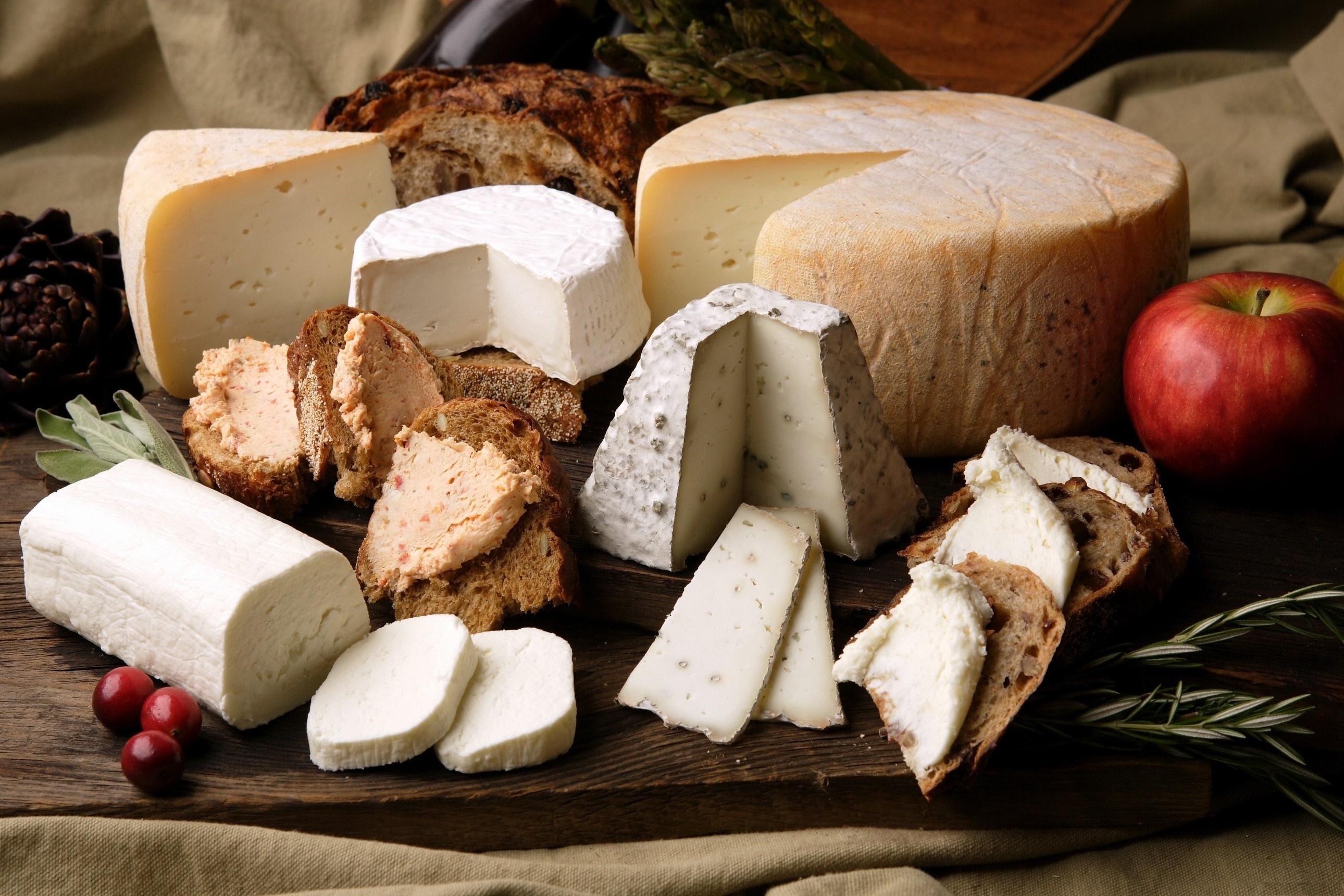 Assortment of cheeses, bread, and fruit on a wooden board HD Wallpaper