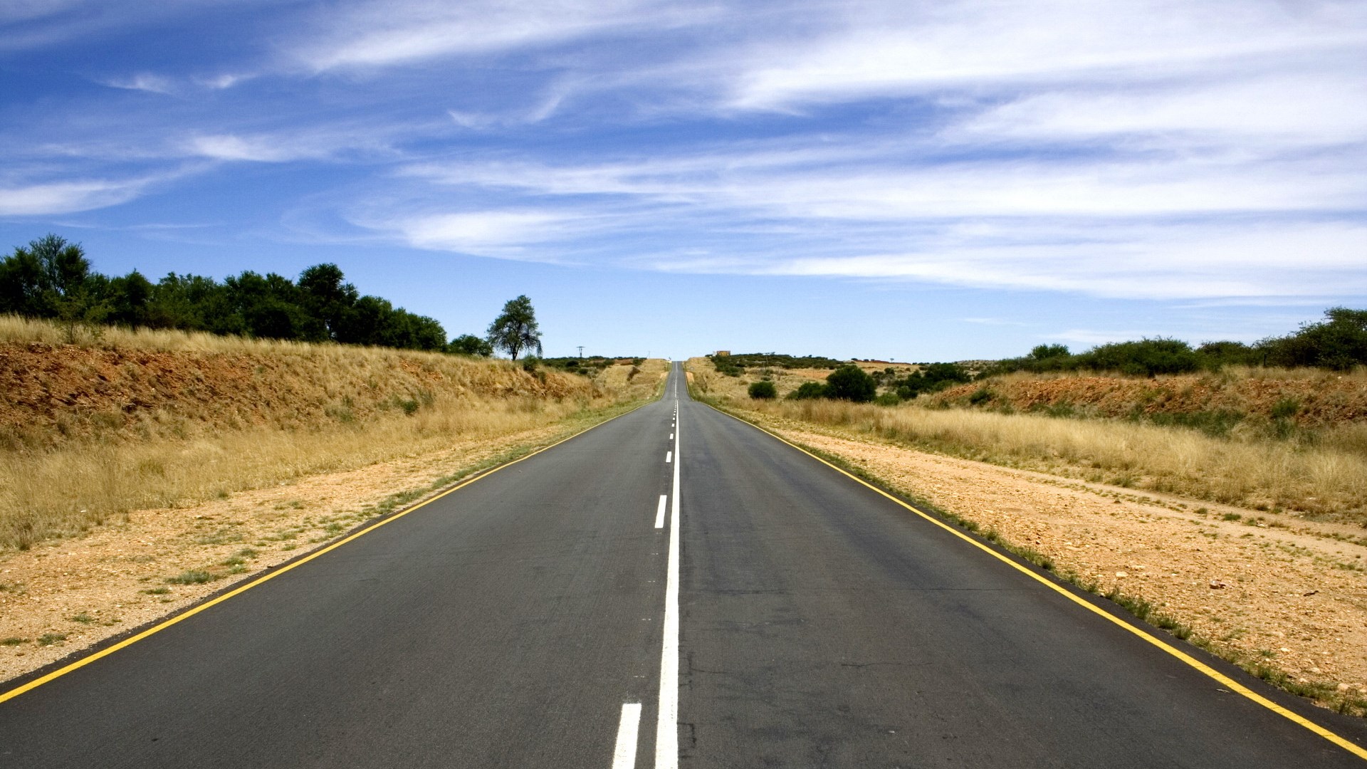 Empty road through a dry landscape under a blue sky HD Wallpaper