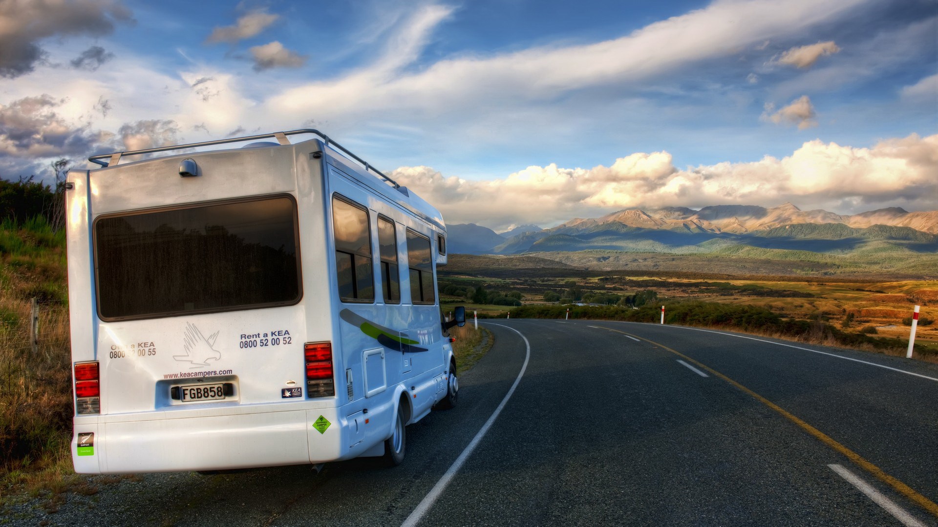 White campervan parked on a winding road with mountains HD Wallpaper