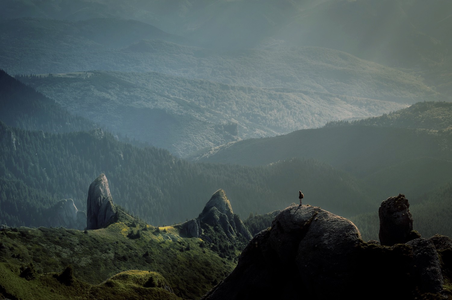 Hiker on a rocky mountain peak overlooking a misty valley HD Wallpaper