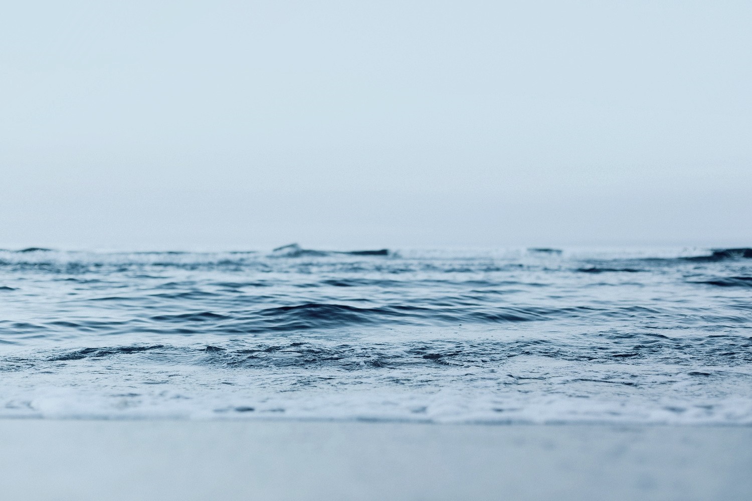Ocean waves rolling onto a sandy shore under a clear sky HD Wallpaper