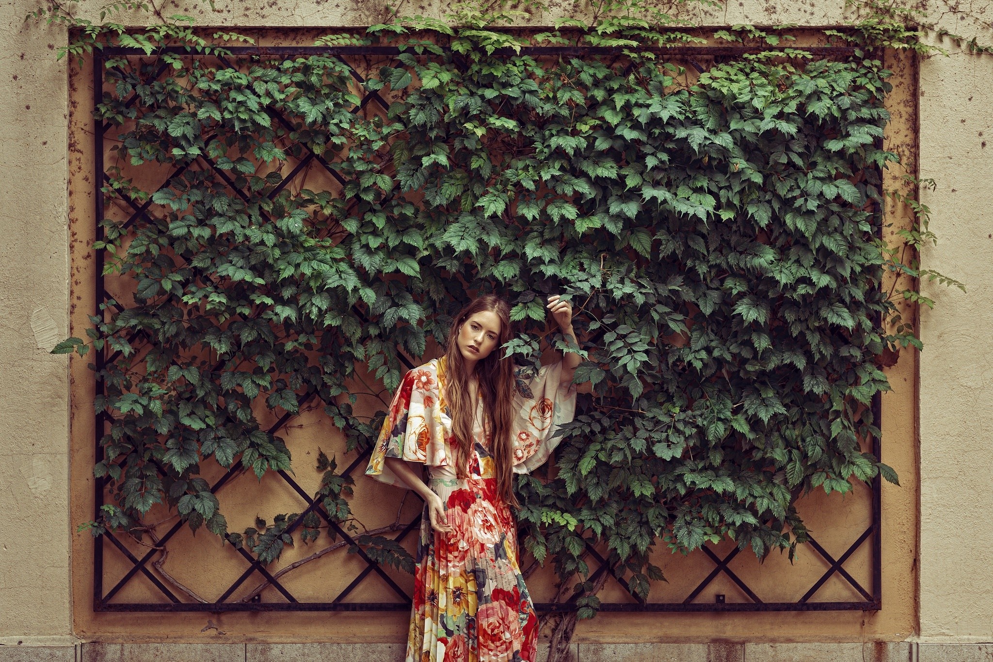 Woman in floral dress standing against ivy-covered wall HD Wallpaper