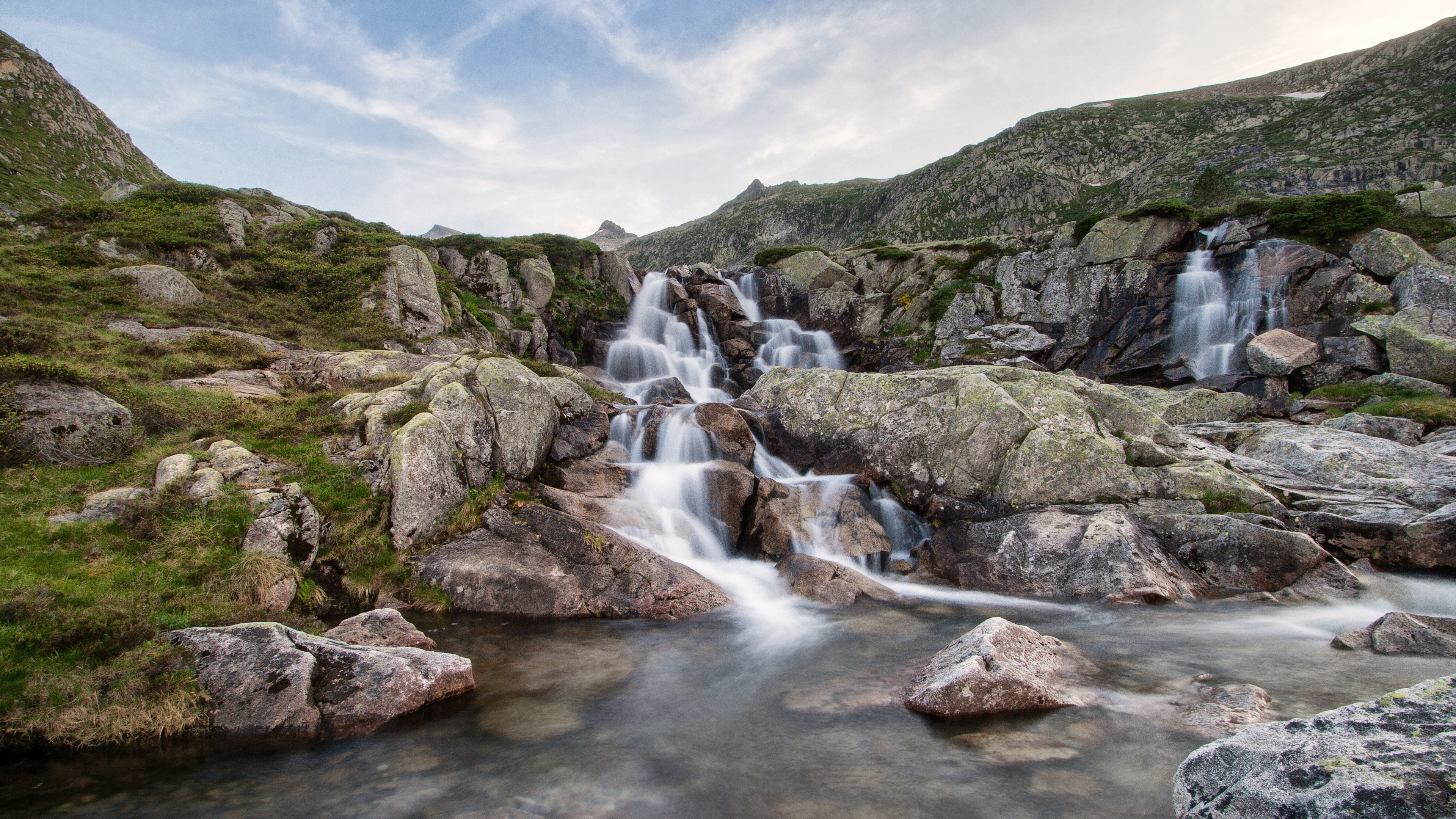 Mountain waterfall flowing over rocks in a natural landscape HD Wallpaper