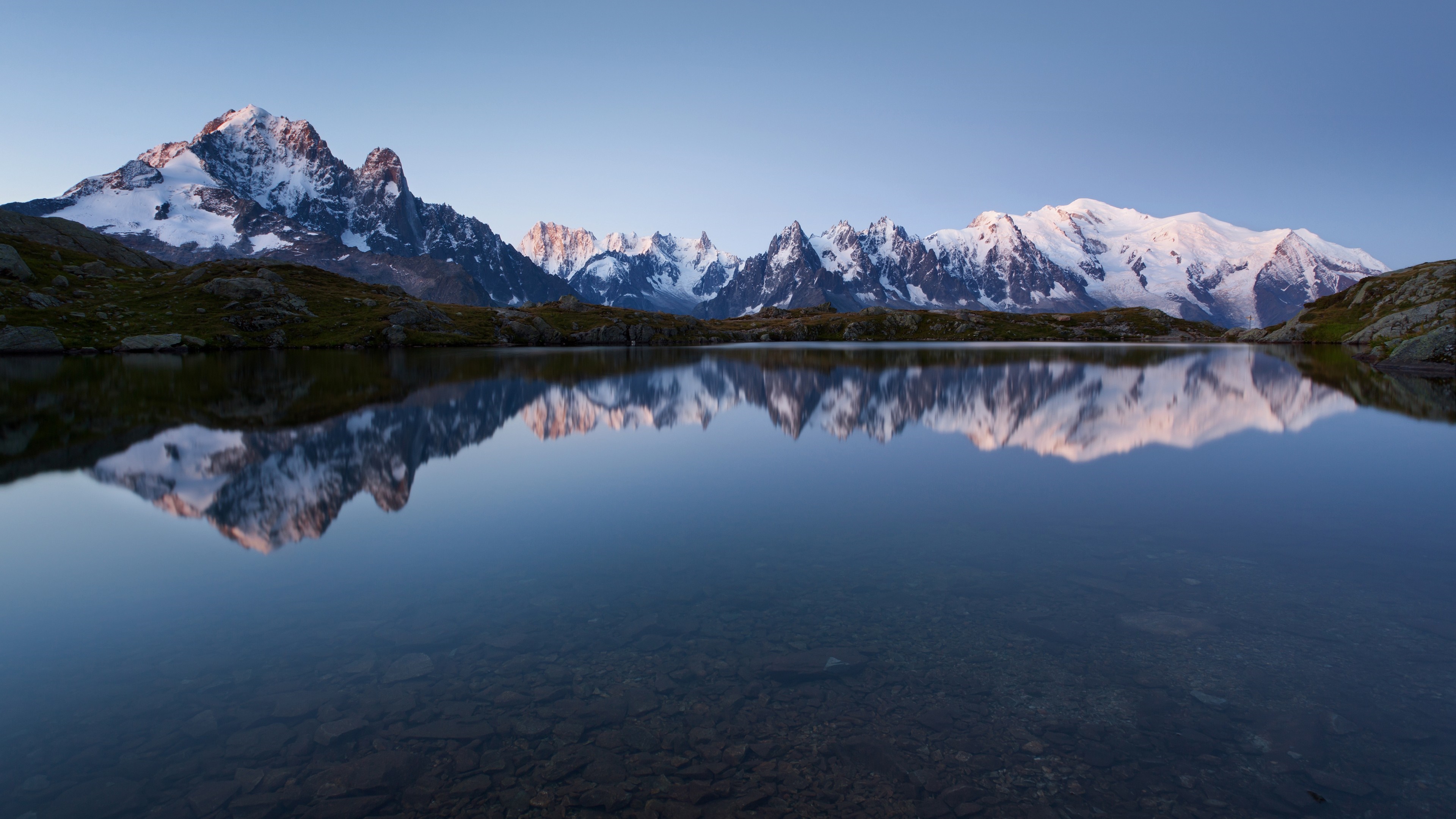 Snow-capped mountains reflected in a calm lake at sunrise HD Wallpaper