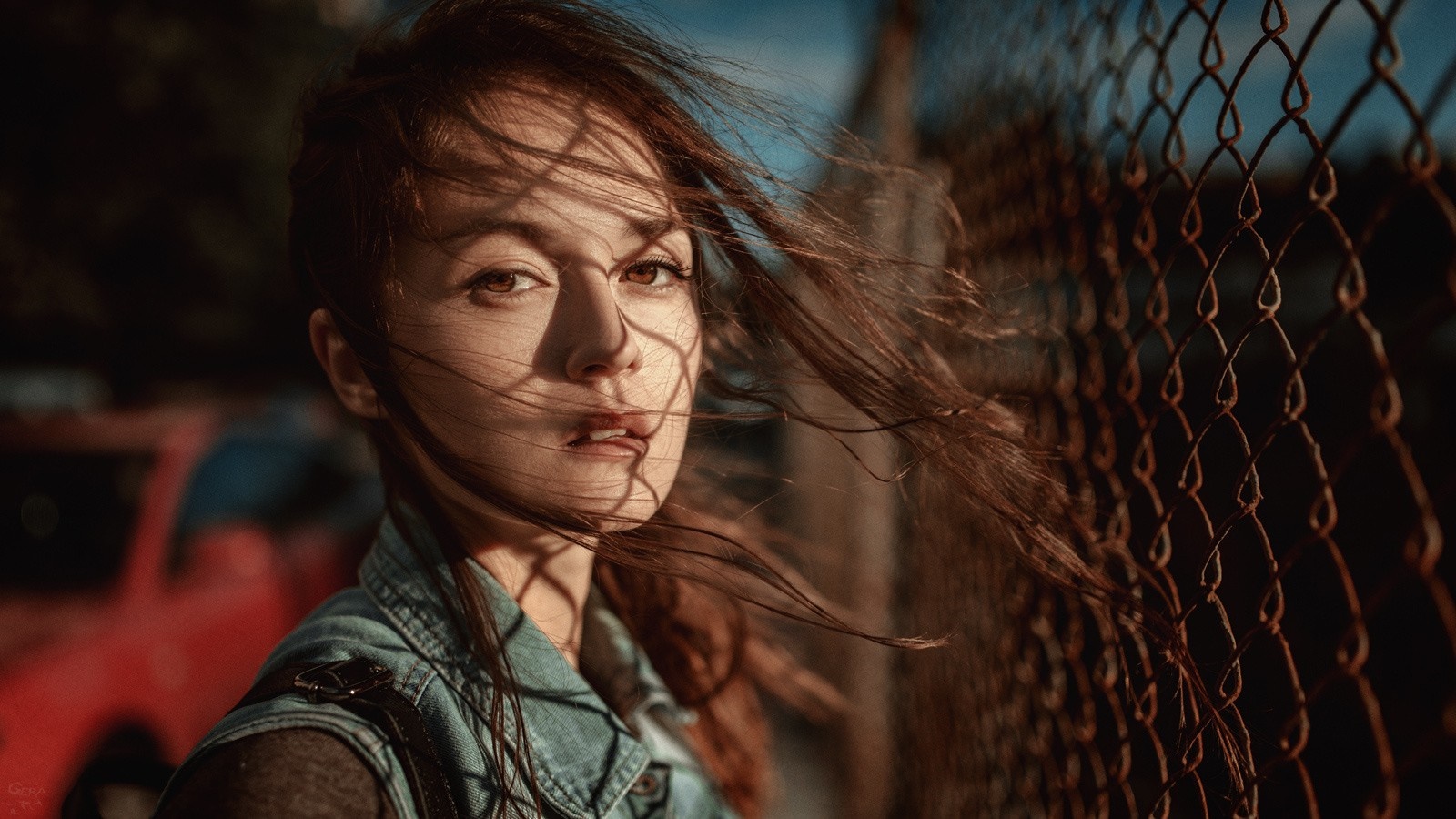Woman with auburn hair in the wind near a fence HD Wallpaper