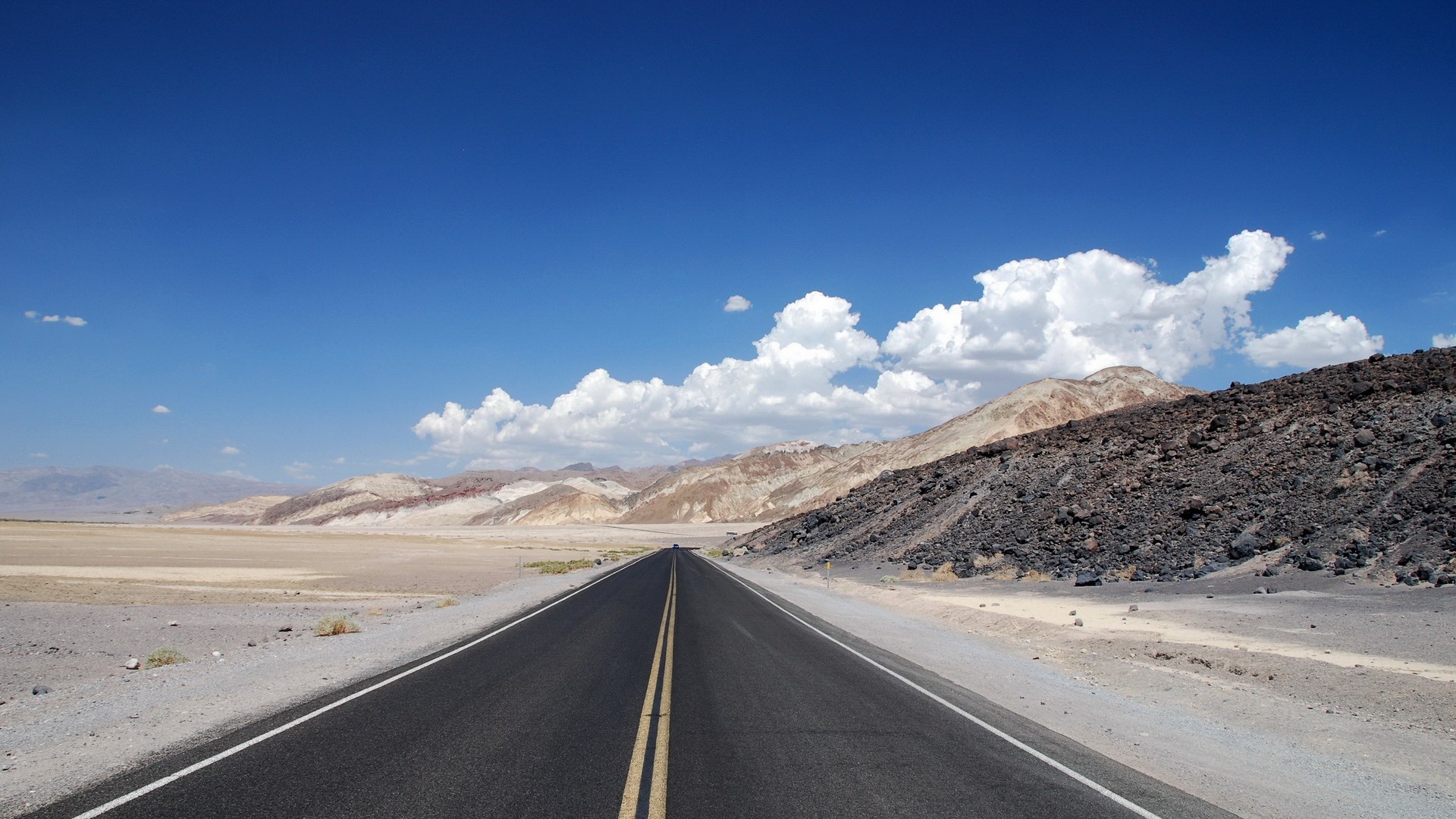 Desert road leading to colorful mountains under blue sky HD Wallpaper