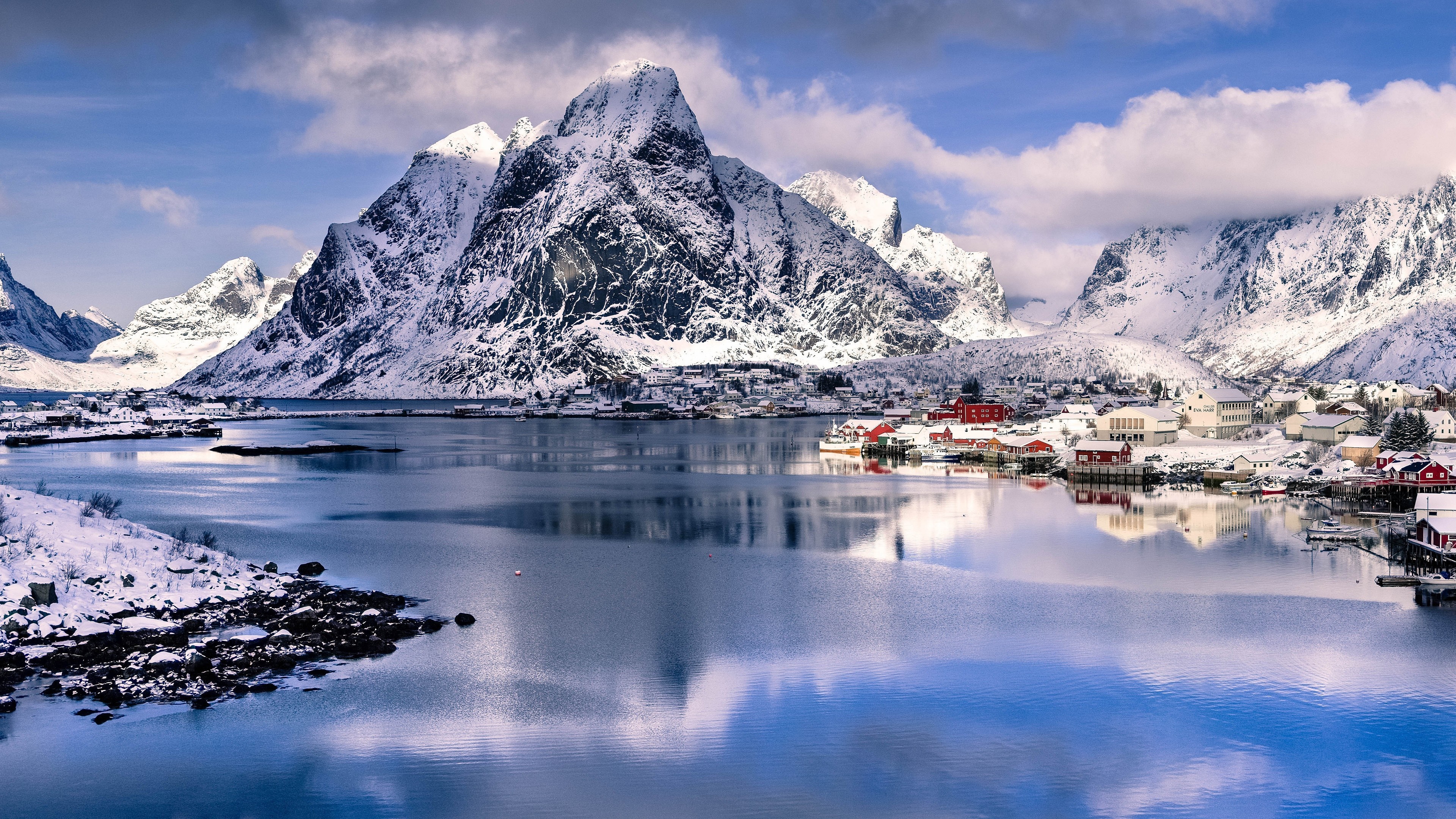 Snowy mountains reflected in a calm lake with a village HD Wallpaper