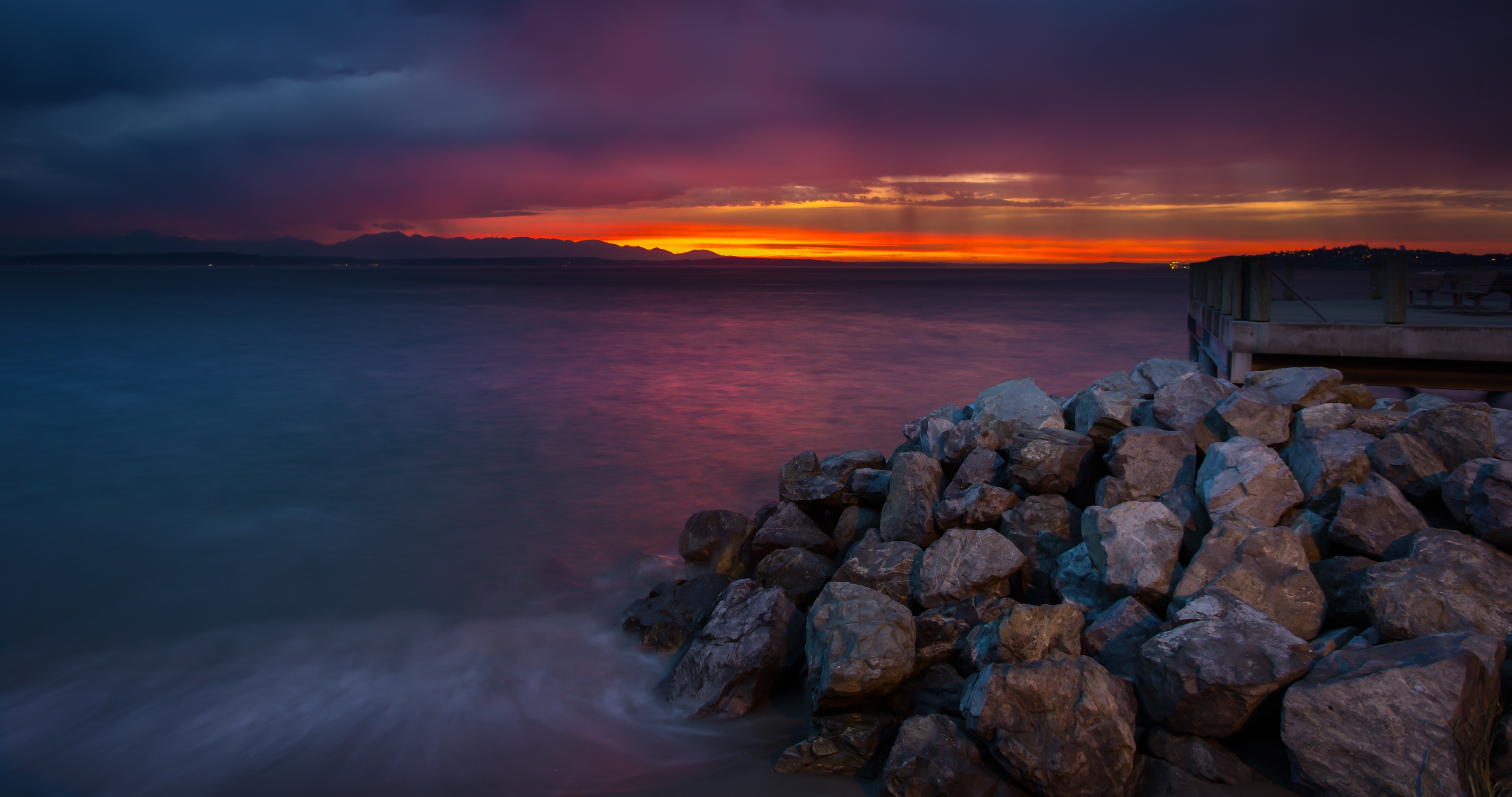 Sunset over the ocean with rocks and a pier HD Wallpaper