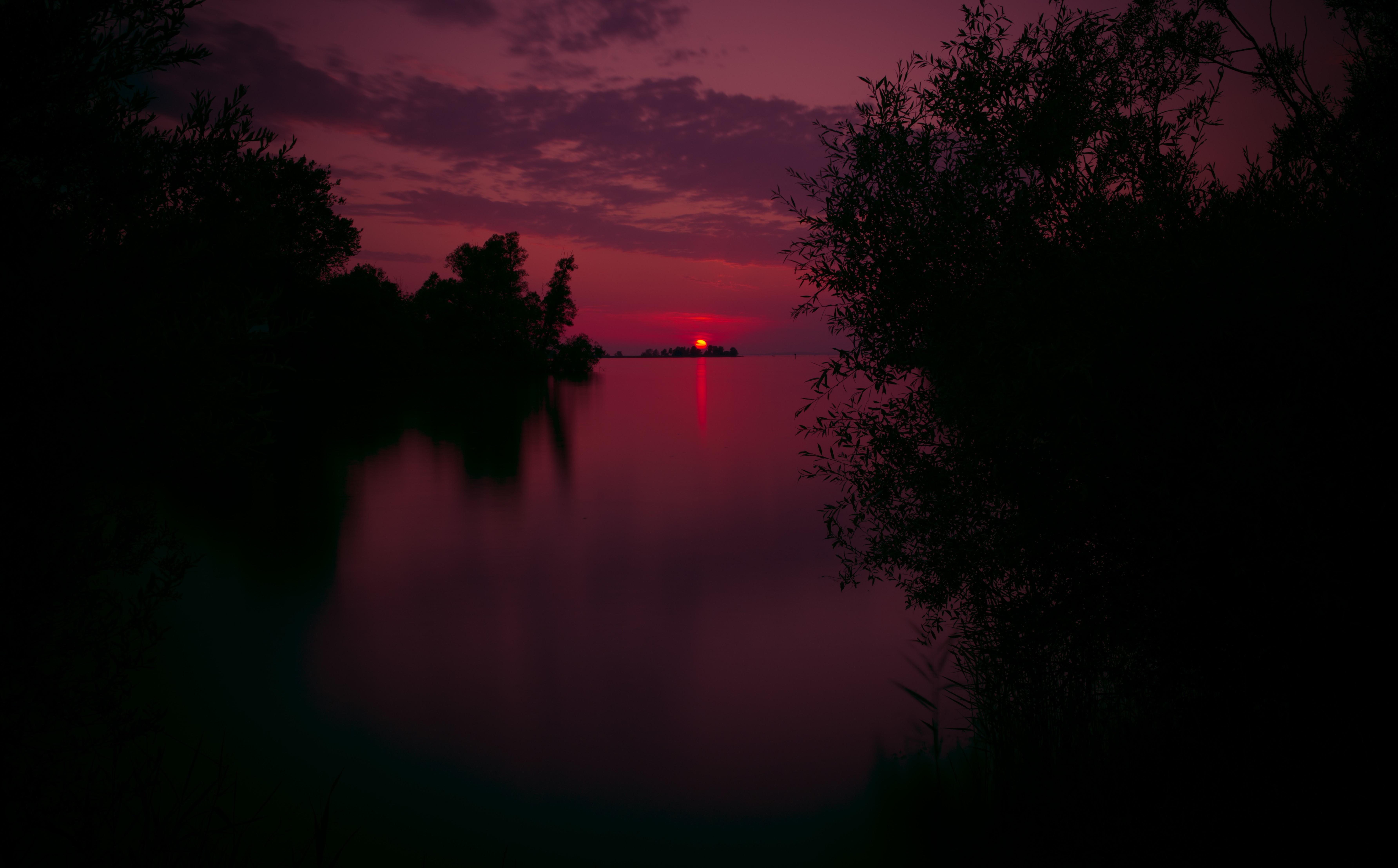 Sunset over a calm lake with silhouetted trees HD Wallpaper