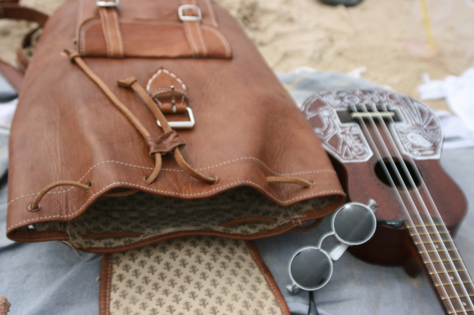 Leather backpack, ukulele, and sunglasses on the beach HD Wallpaper