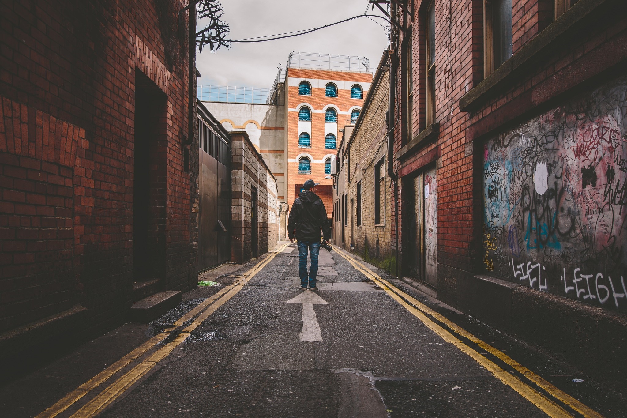 Man walking down a graffiti-covered alleyway in a city HD Wallpaper