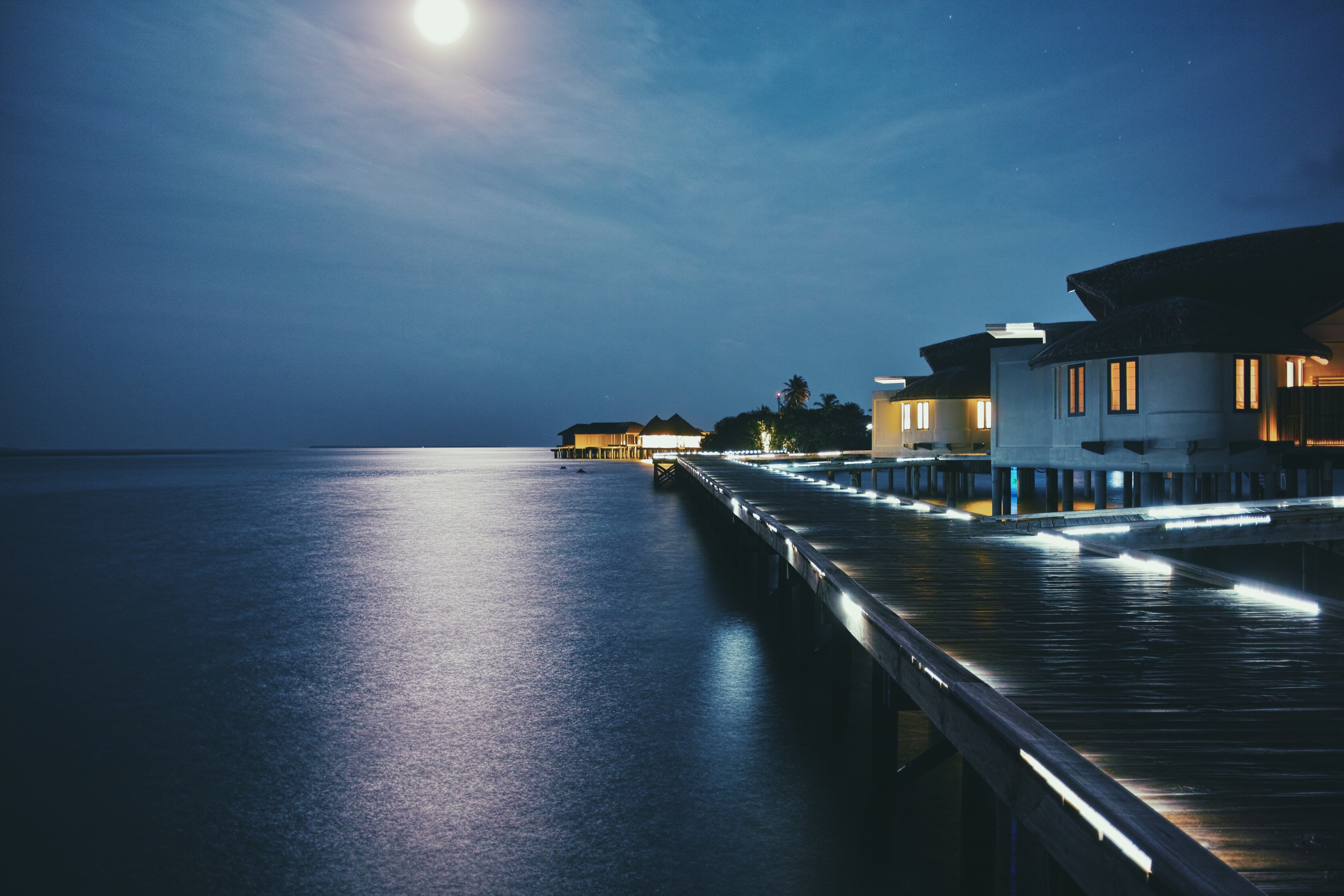 Overwater bungalows at night with moon reflection on the sea HD Wallpaper