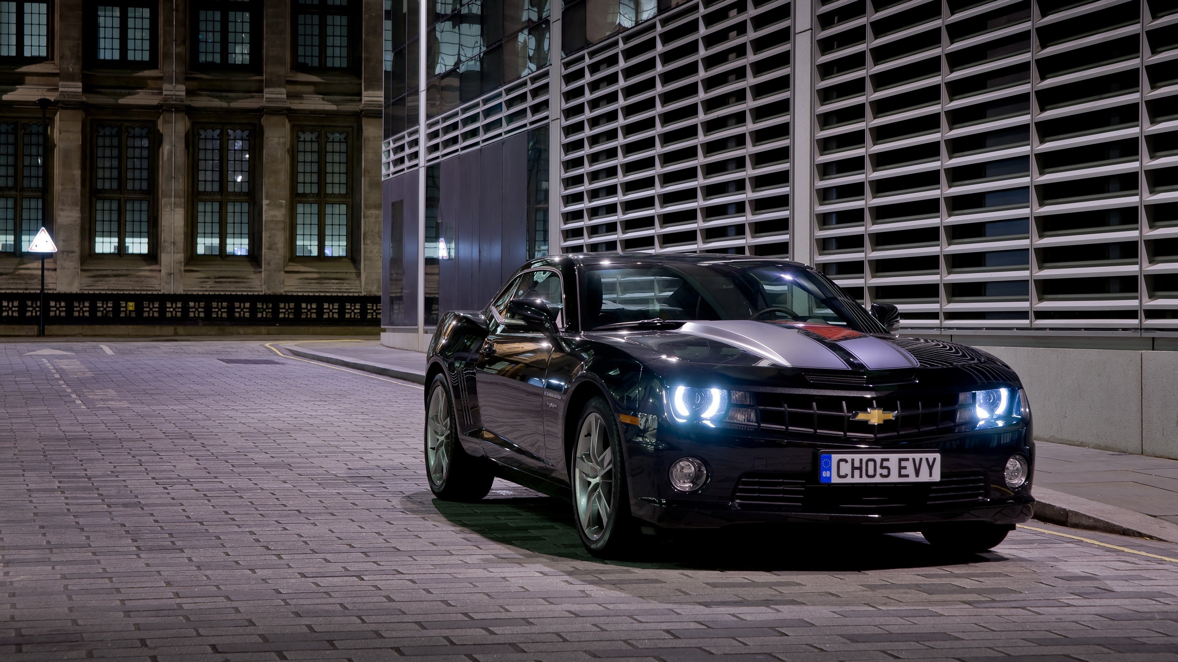 Black Chevrolet Camaro parked on cobblestone street at night HD Wallpaper