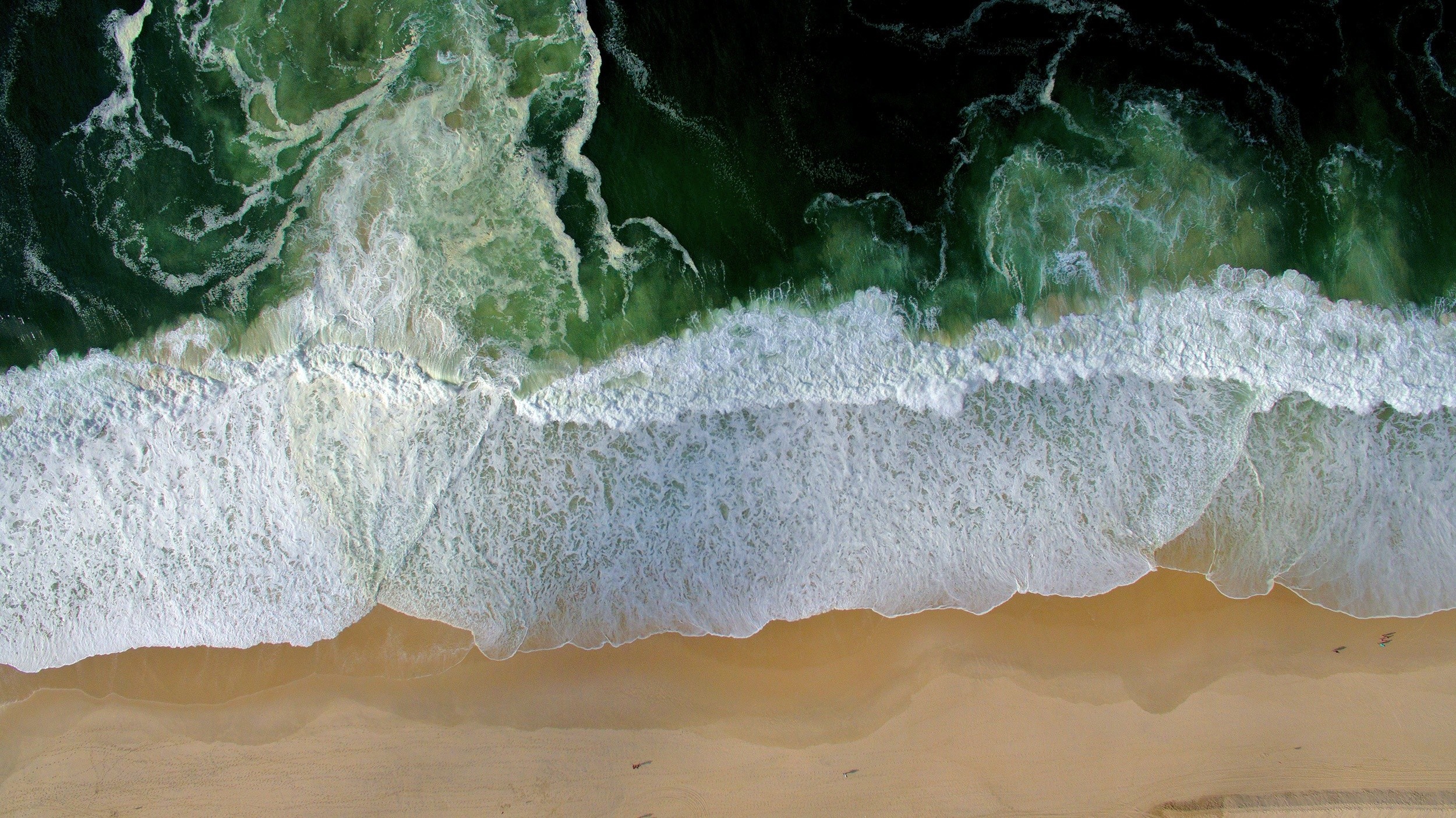 Aerial view of ocean waves crashing on a sandy beach HD Wallpaper