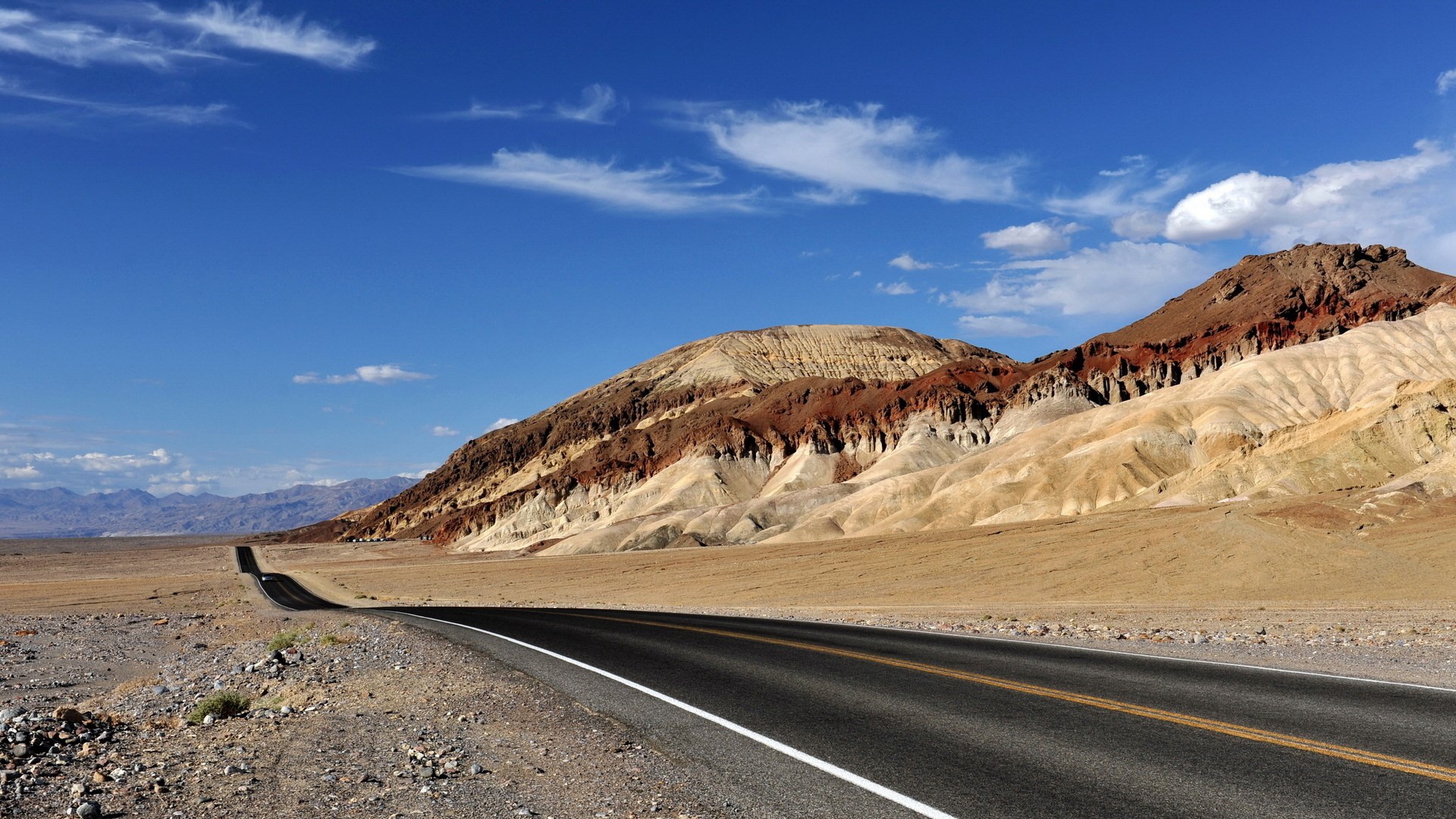 Desert road leading to colorful mountains under a blue sky HD Wallpaper