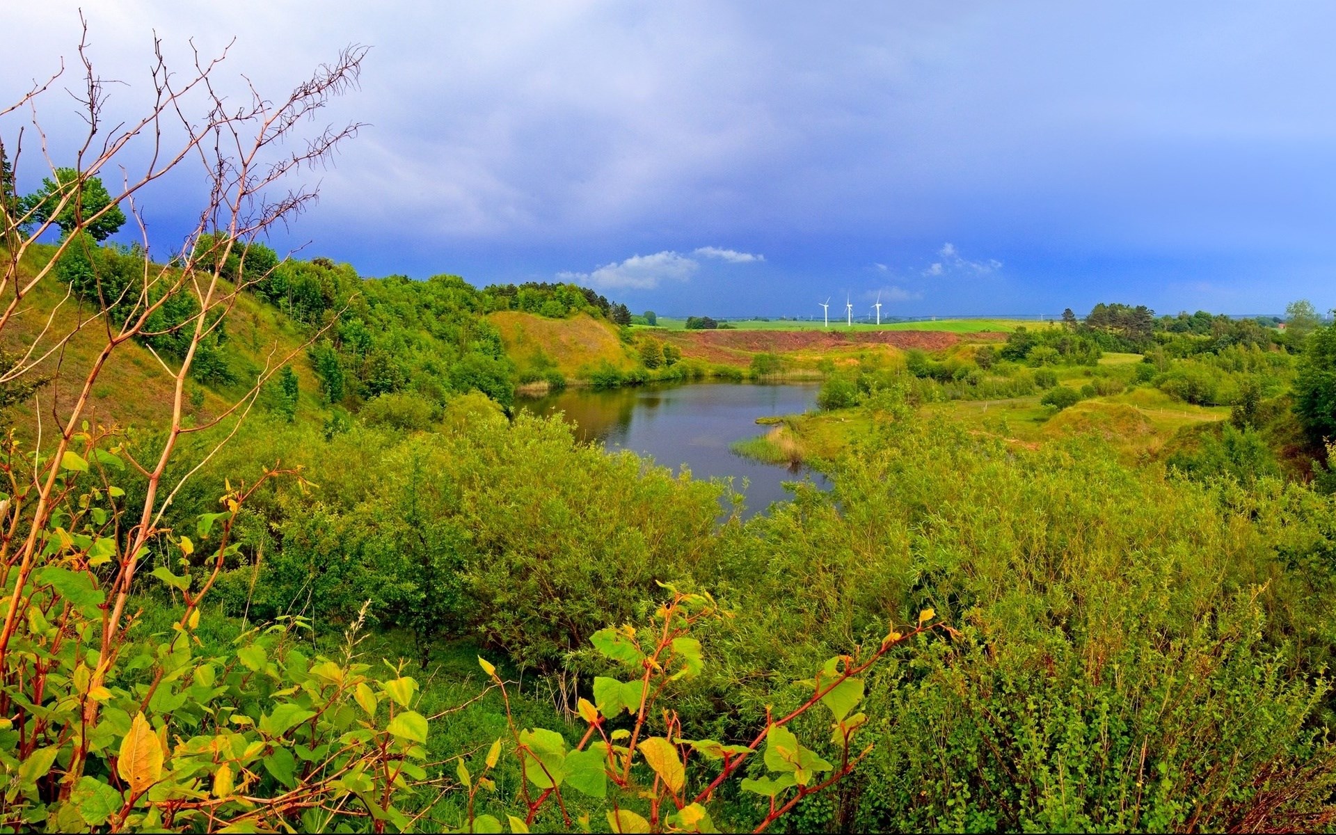 Wind turbines in a green landscape with a lake HD Wallpaper