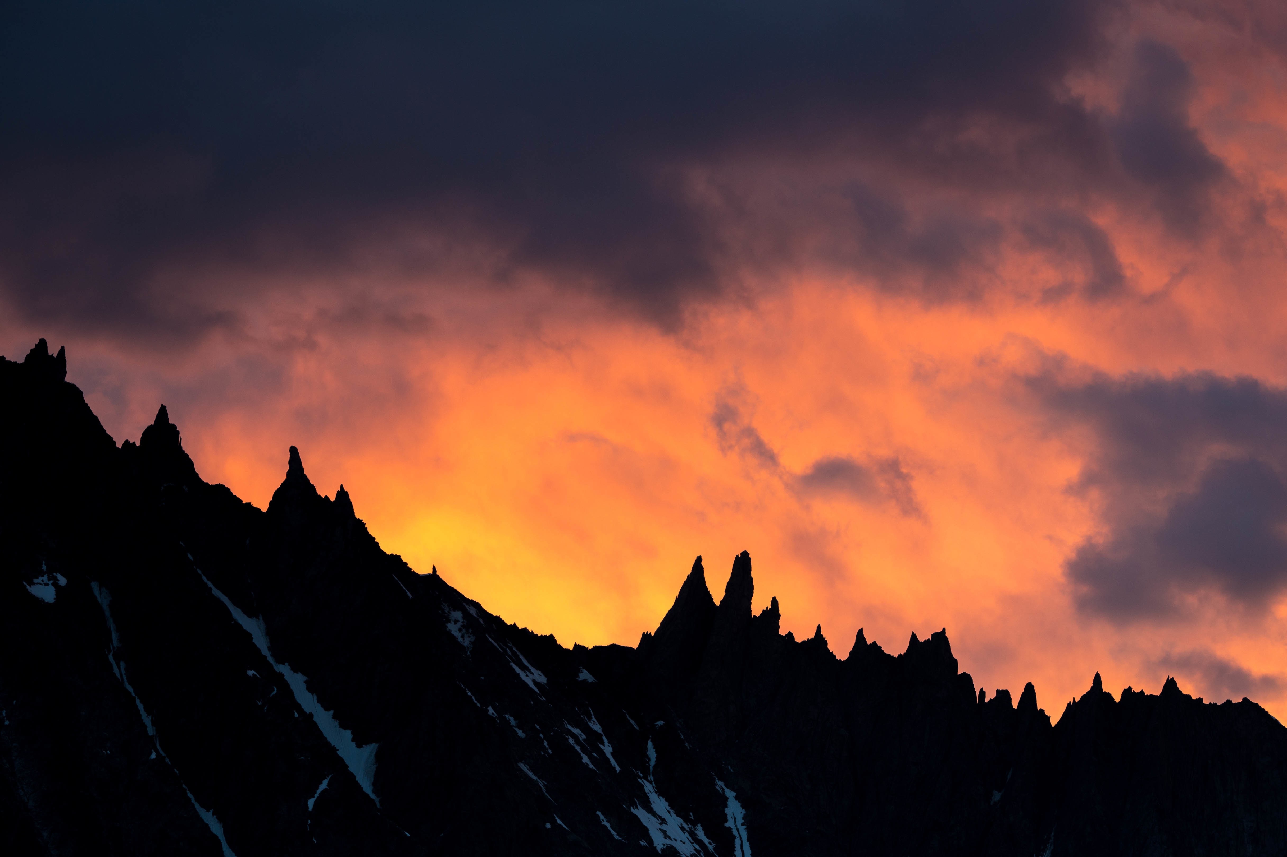 Silhouette of jagged mountains against a fiery sunset sky HD Wallpaper