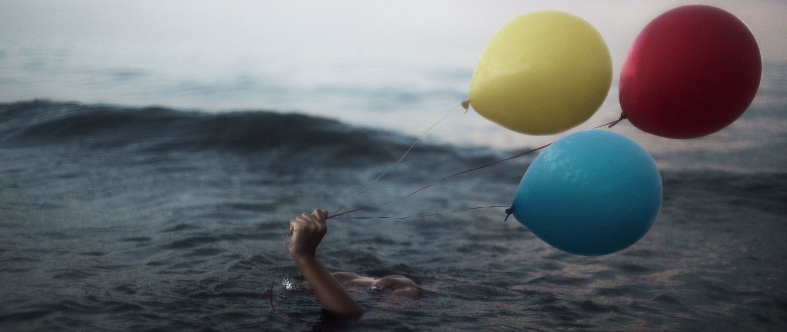 Person drowning in sea holding balloons HD Wallpaper