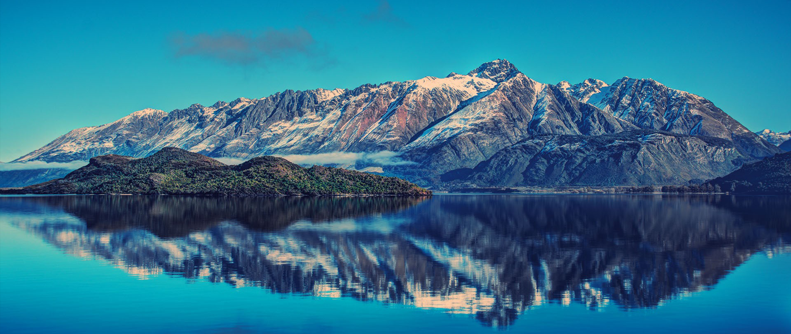 Snow-capped mountains reflected in a calm lake with an island HD Wallpaper