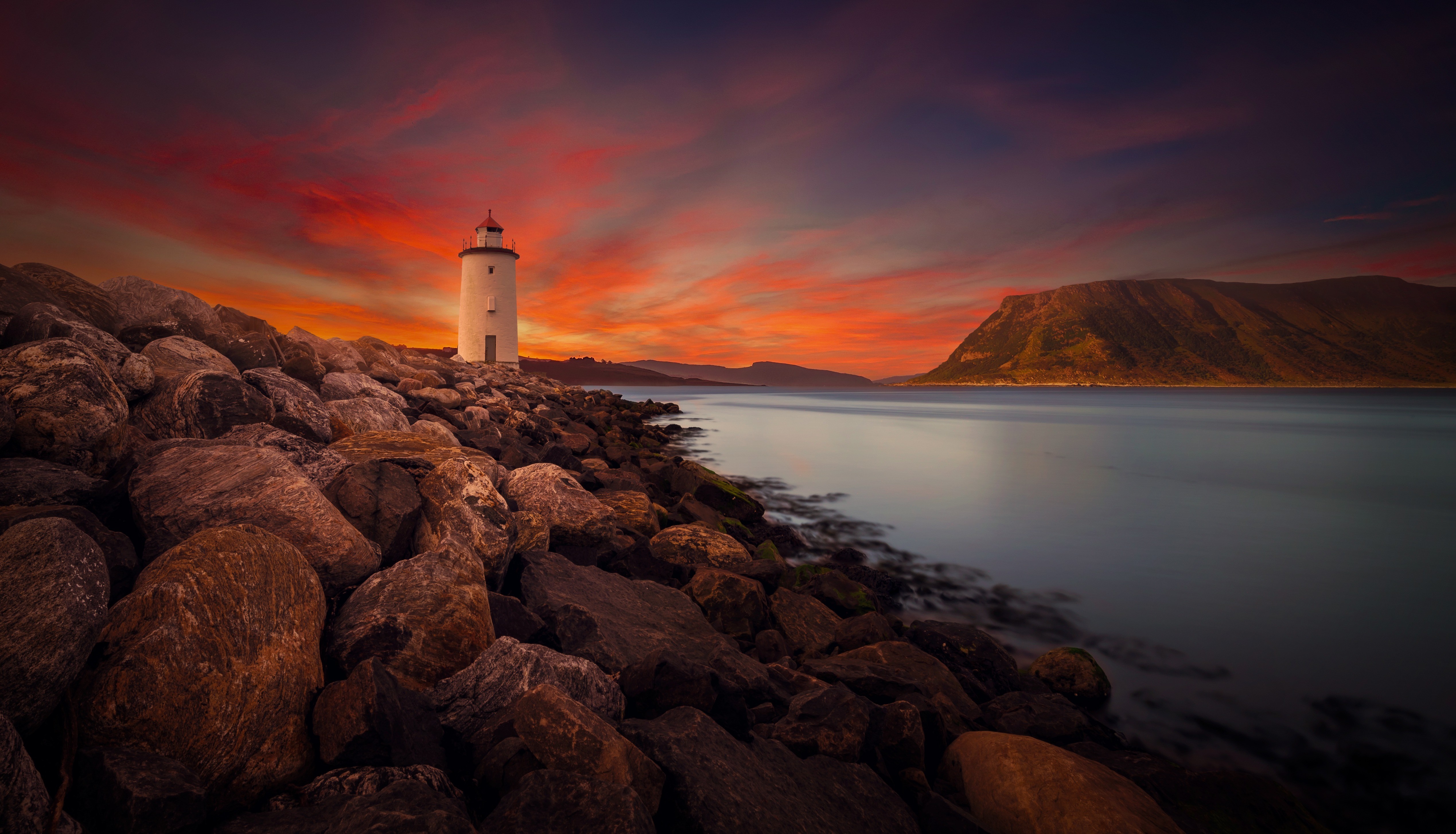 Lighthouse on rocky shore during sunset over the ocean HD Wallpaper