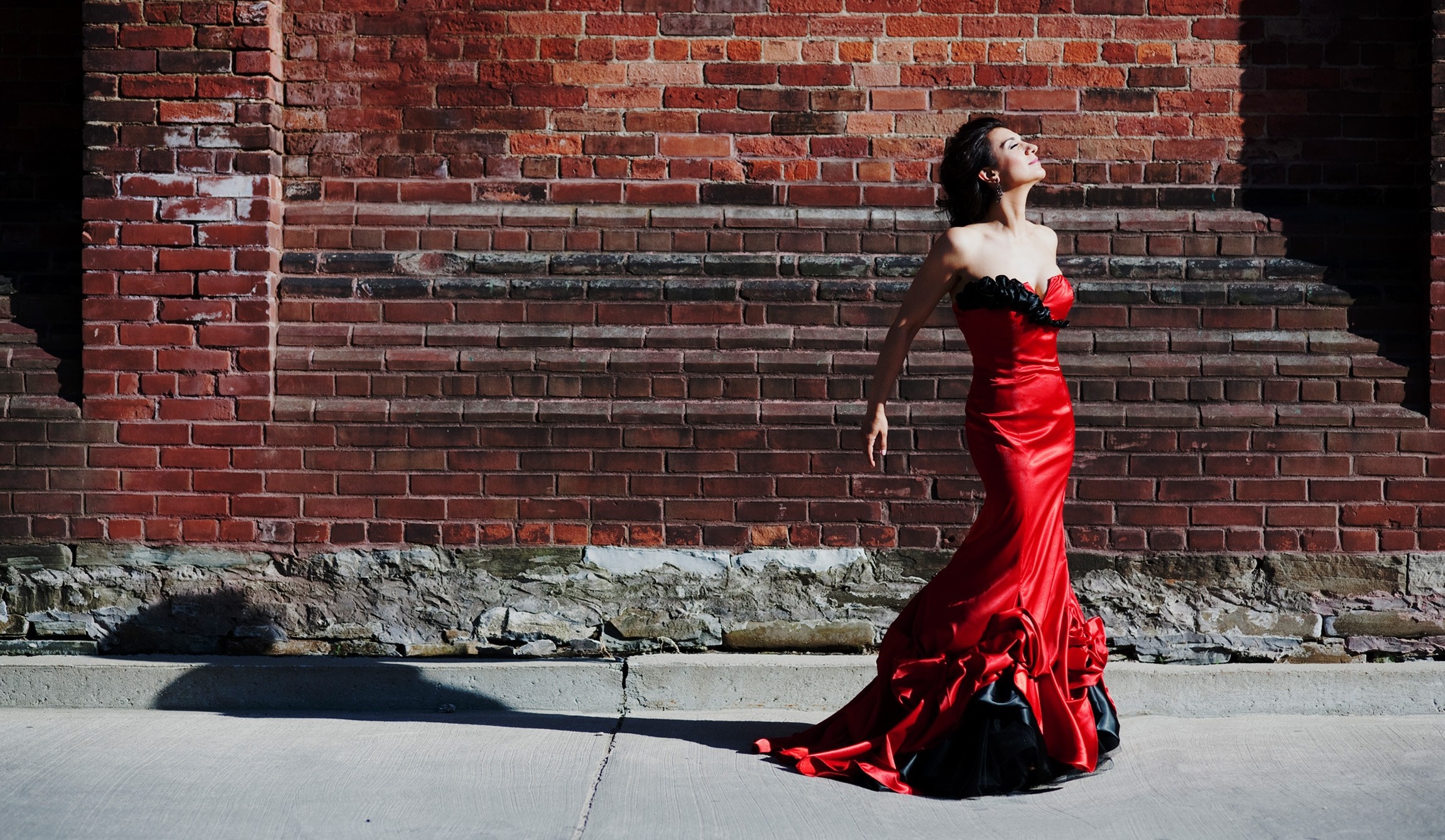 Woman in a red dress posing against a brick wall HD Wallpaper