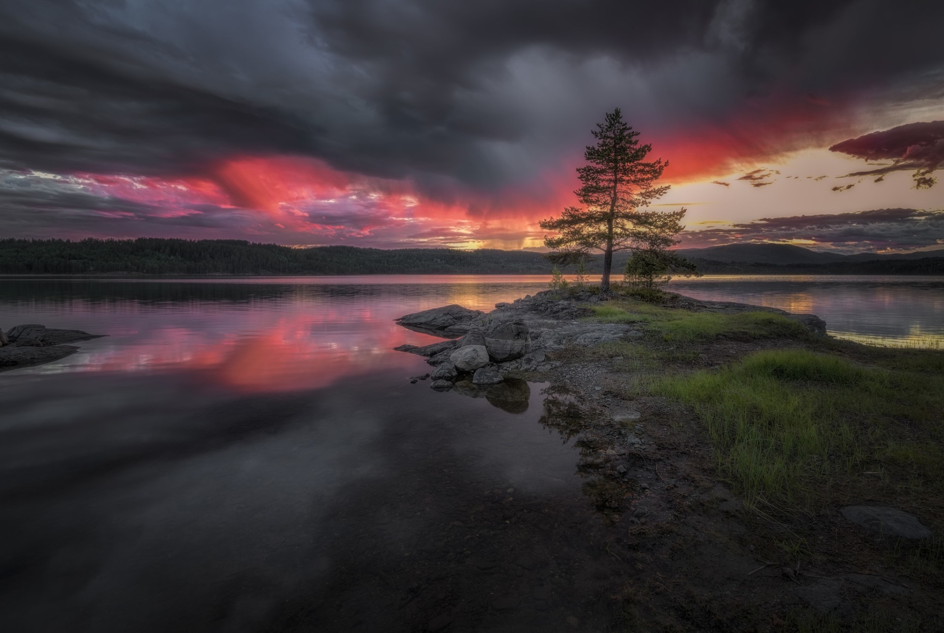 Dramatic sunset over a calm lake with a lone tree on a rocky island HD Wallpaper