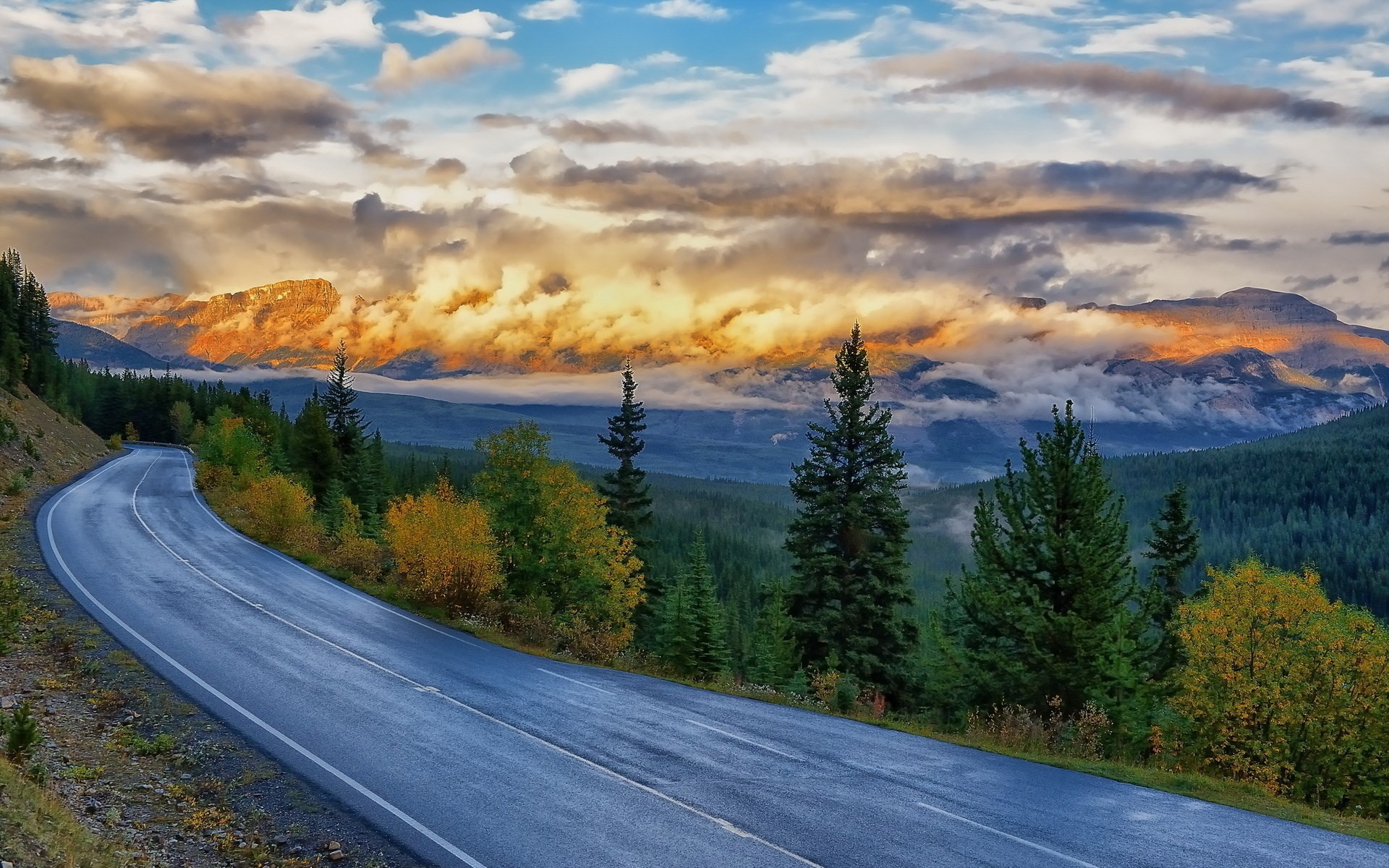 Mountain road with autumn trees and dramatic clouds HD Wallpaper
