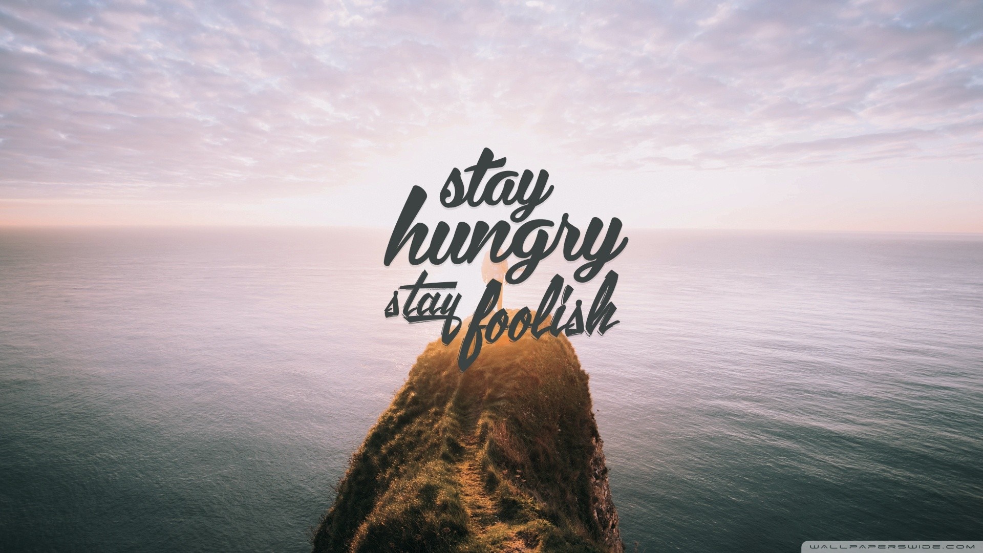 Stay Hungry Stay Foolish quote over ocean cliff at sunset HD Wallpaper