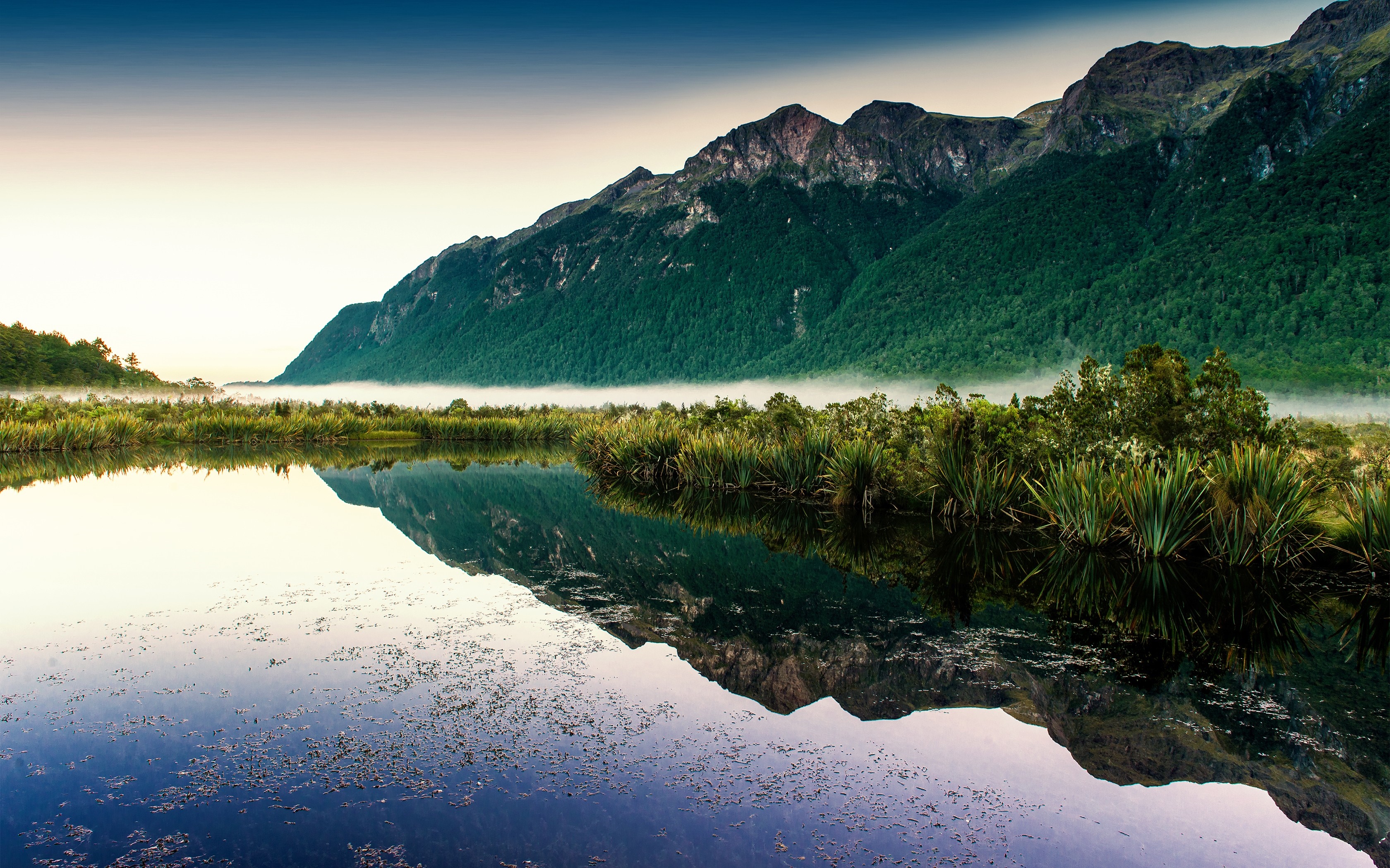 Misty mountains reflected in a calm lake at dawn HD Wallpaper