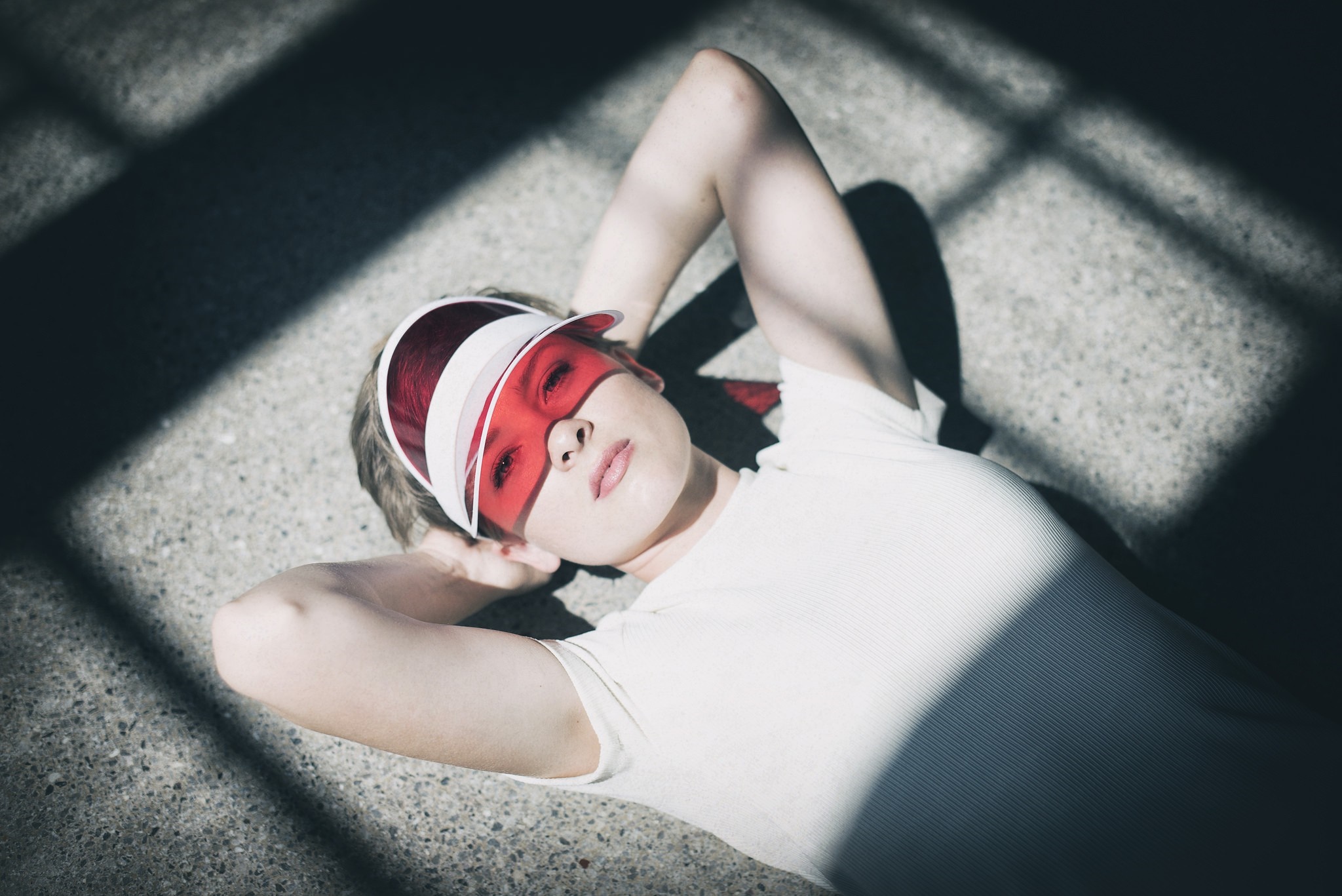 Woman wearing red visor lying on concrete with shadows HD Wallpaper