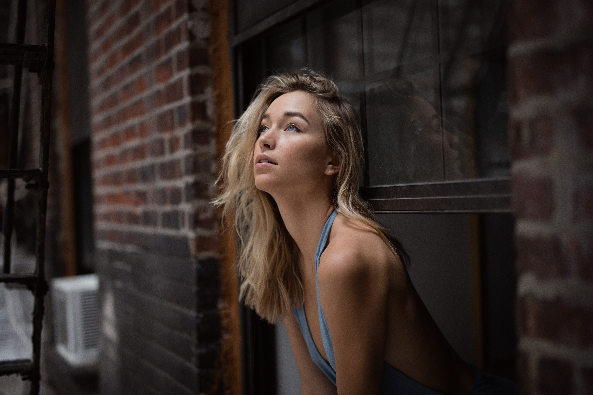 Woman with blonde hair looking up by a brick building HD Wallpaper
