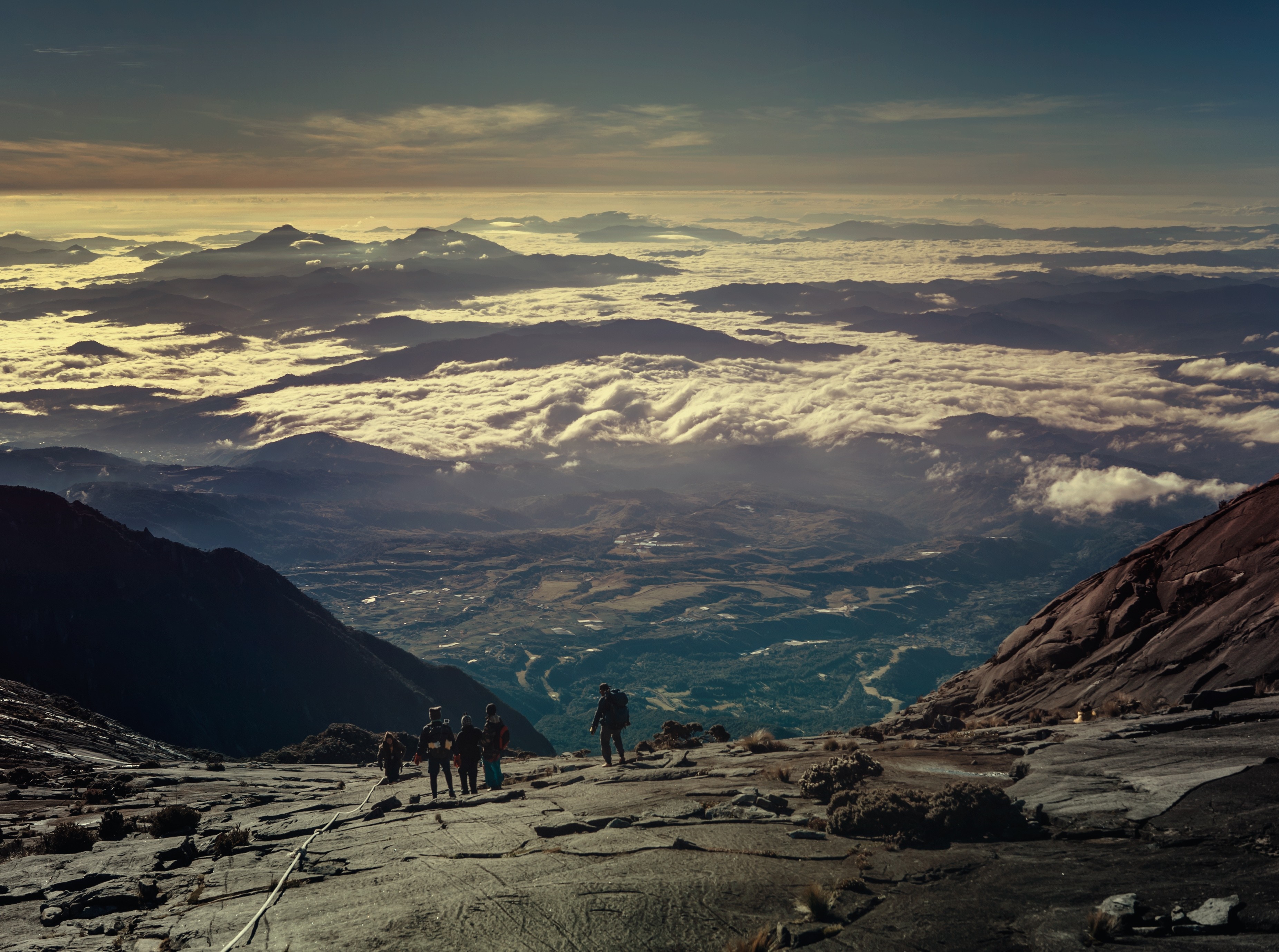Hikers on a rocky mountain slope above a cloud-filled valley at sunrise HD Wallpaper