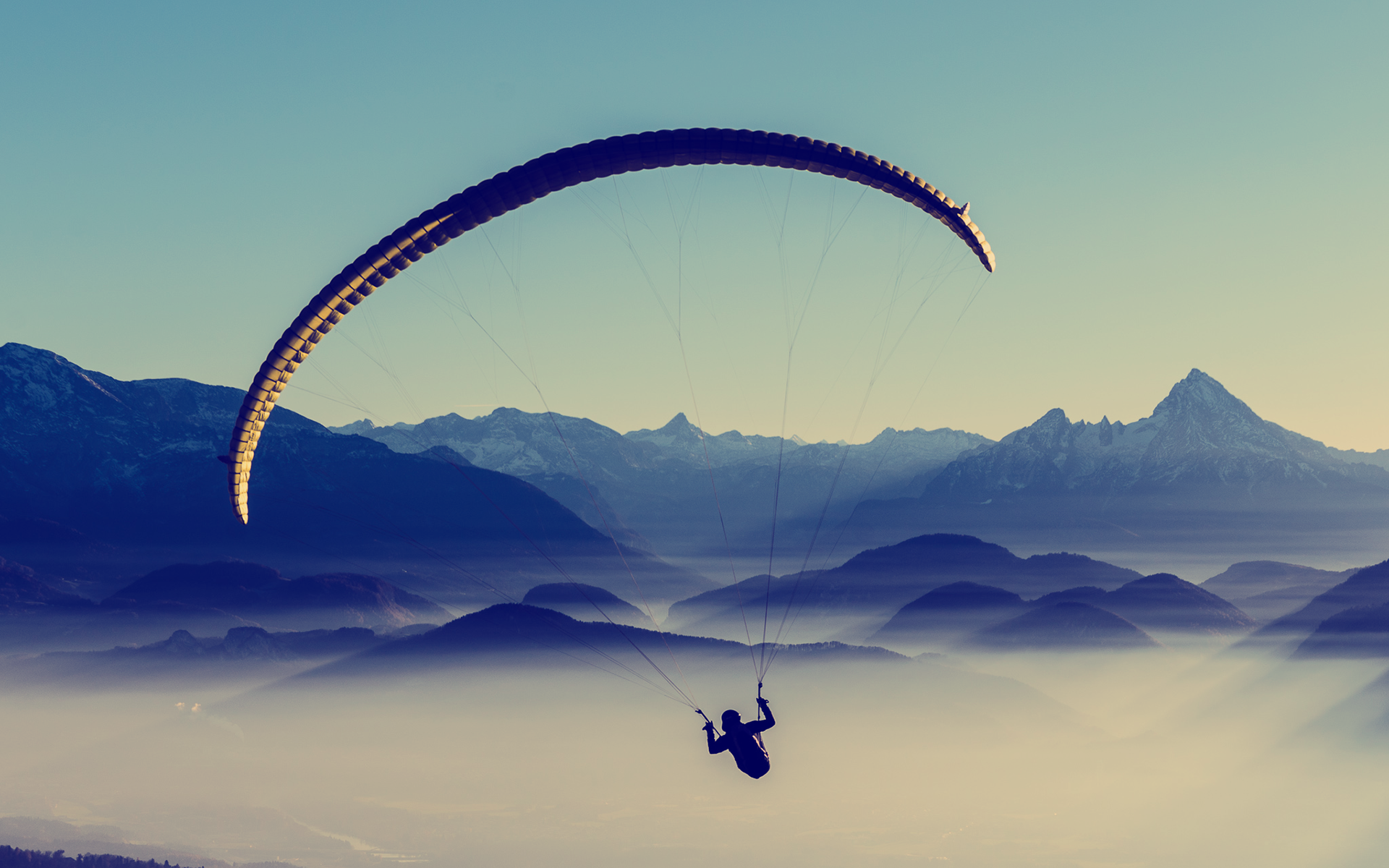 Paraglider flying over misty mountains at sunset HD Wallpaper