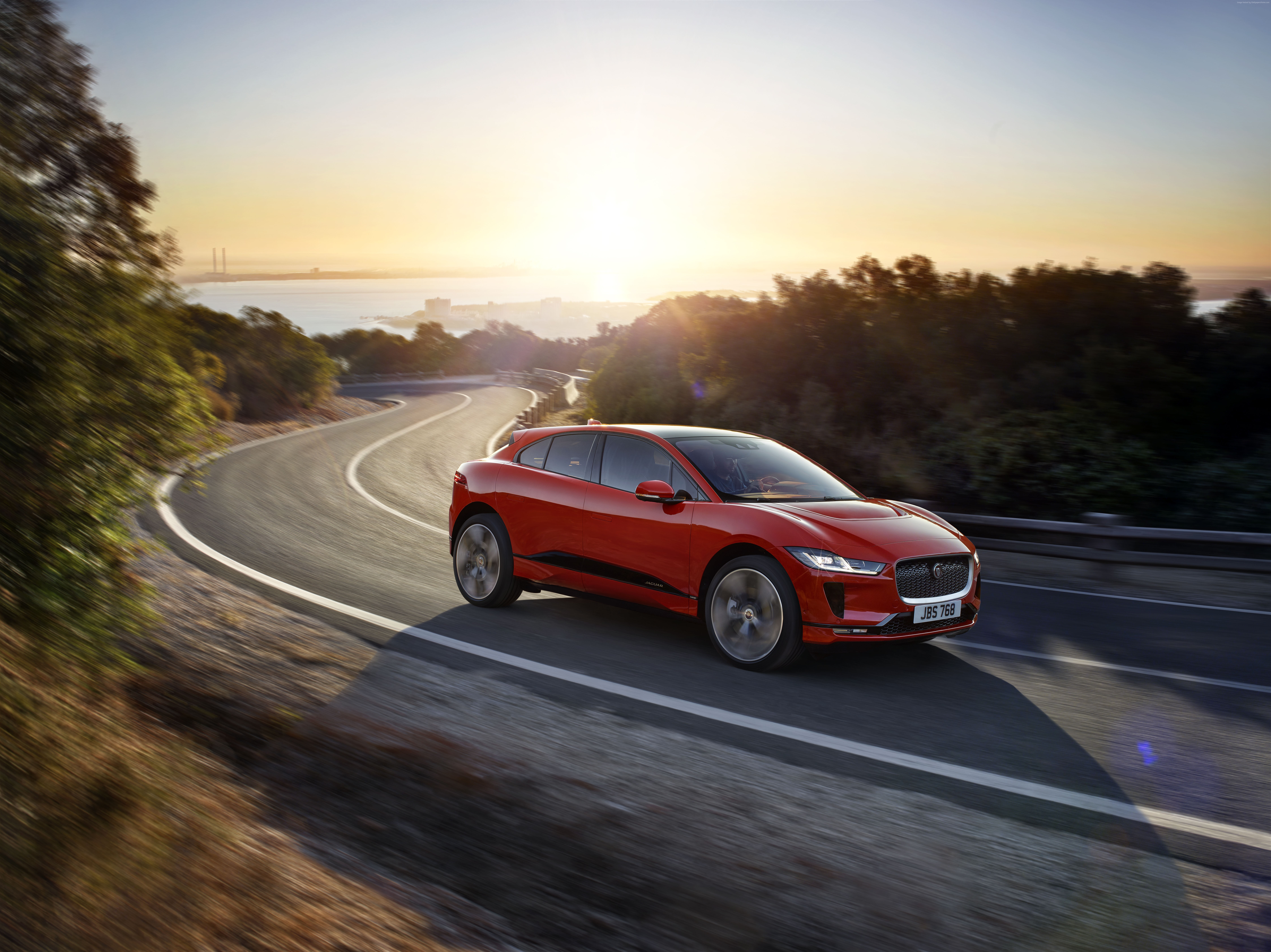 Red Jaguar I-Pace electric car driving on a winding road at sunset HD Wallpaper