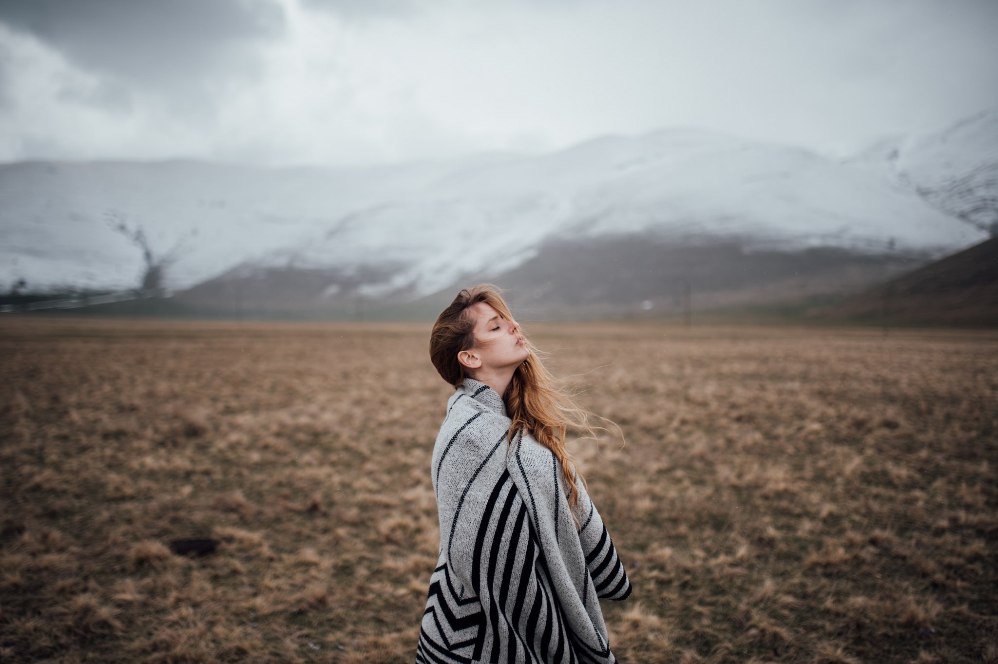 Woman wrapped in blanket in a field with mountains HD Wallpaper