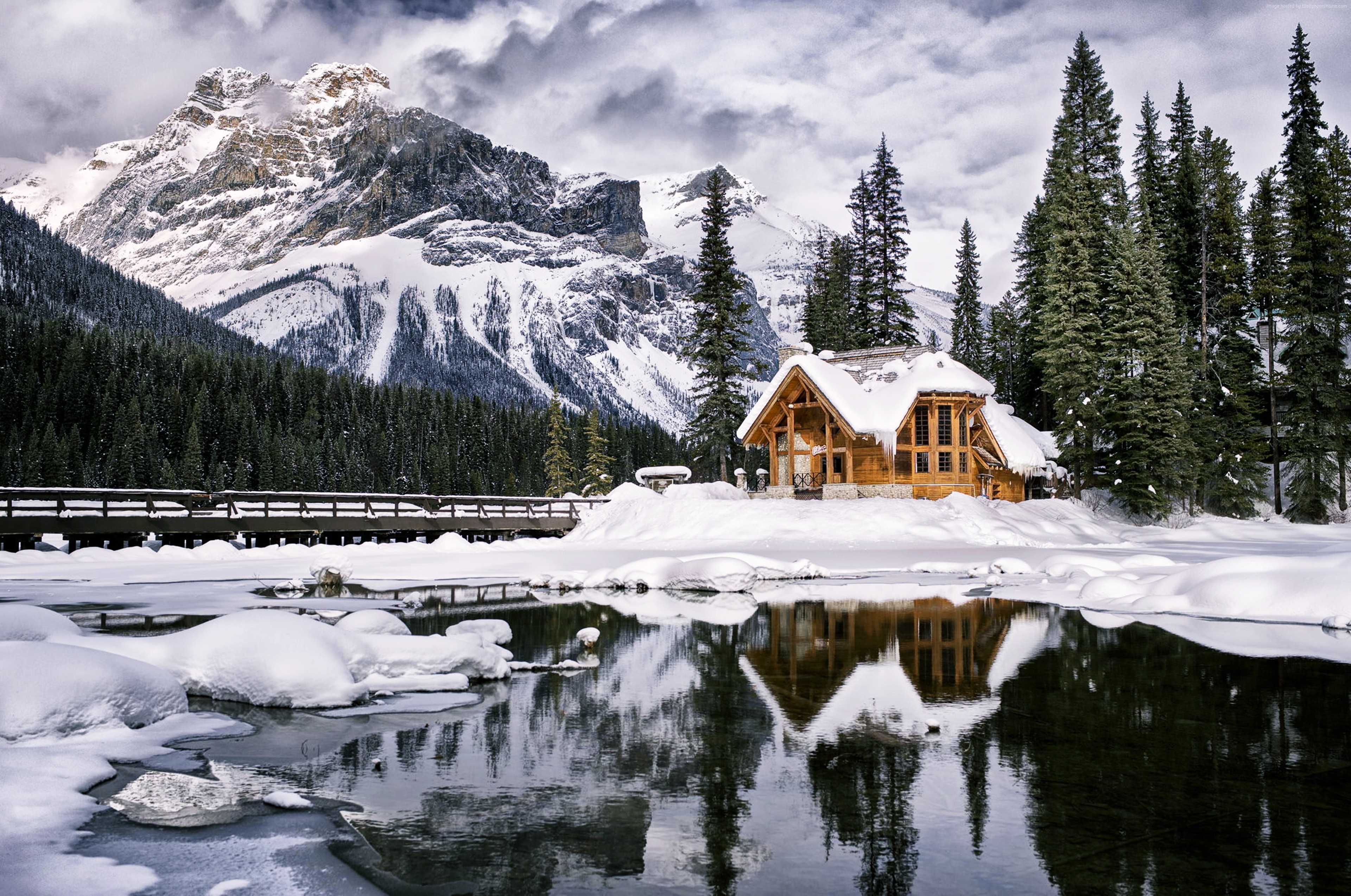 Wooden house by a frozen lake with snowy mountains HD Wallpaper