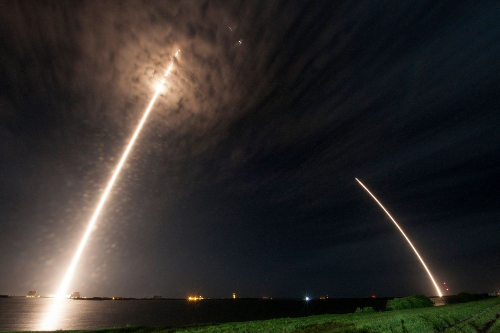 Two rockets launch into the night sky over water HD Wallpaper