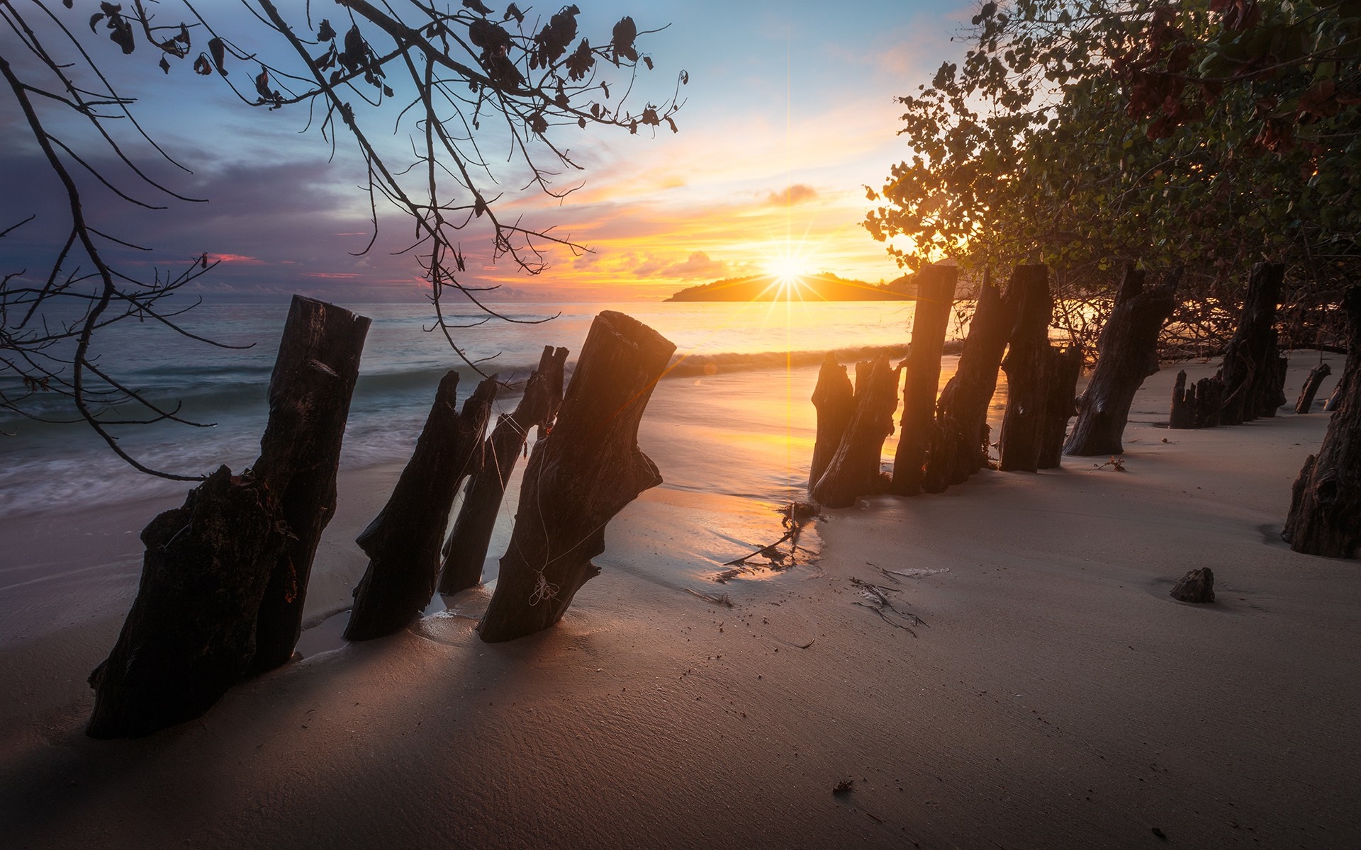 Sunset over the ocean with wooden posts on the beach HD Wallpaper