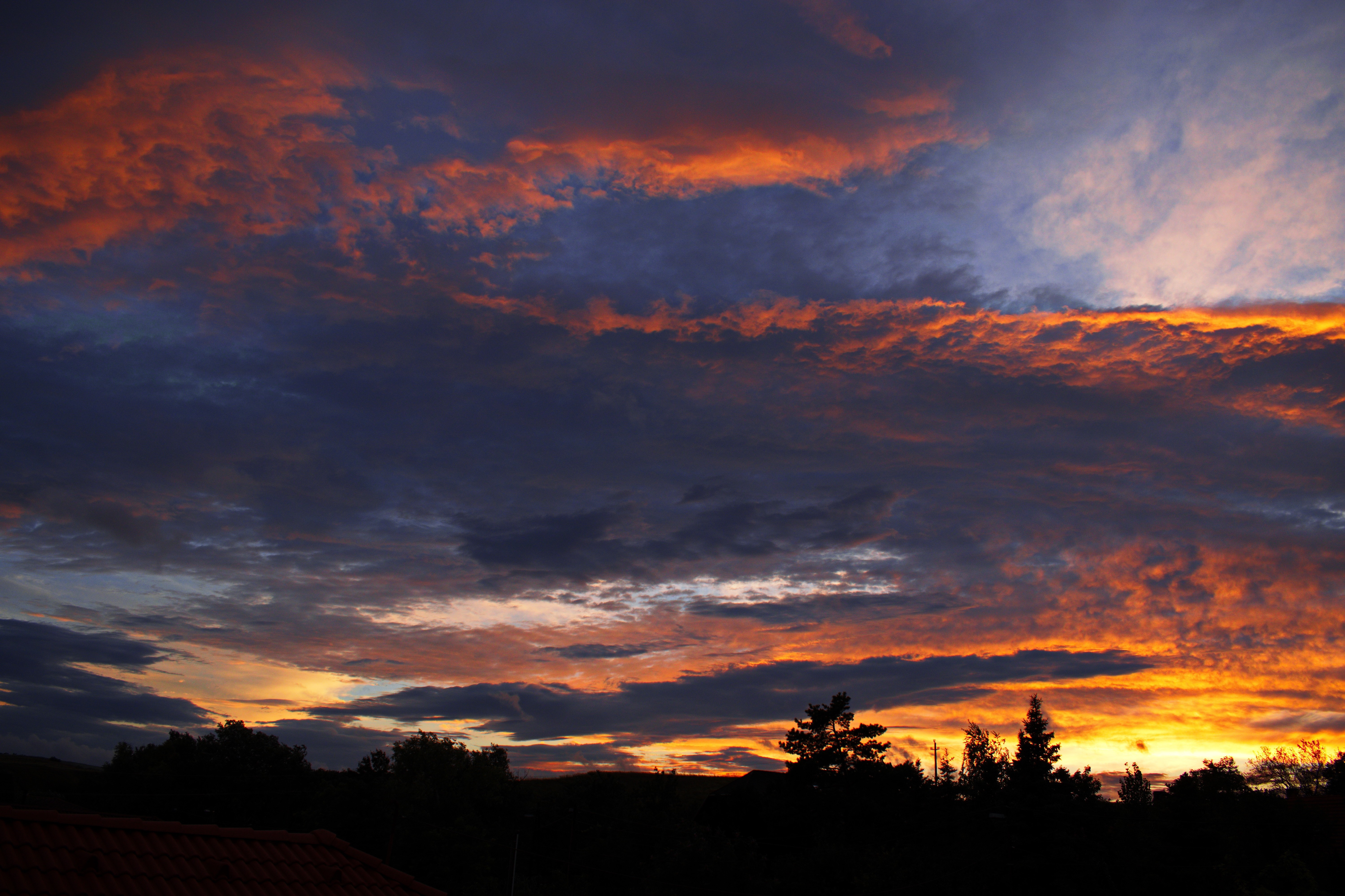 Sunset clouds over silhouetted trees and landscape HD Wallpaper