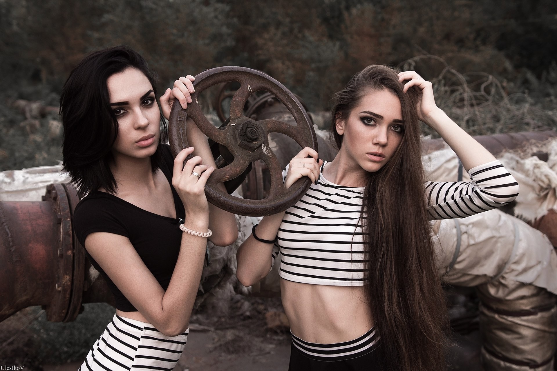 Two women posing with a large valve wheel HD Wallpaper