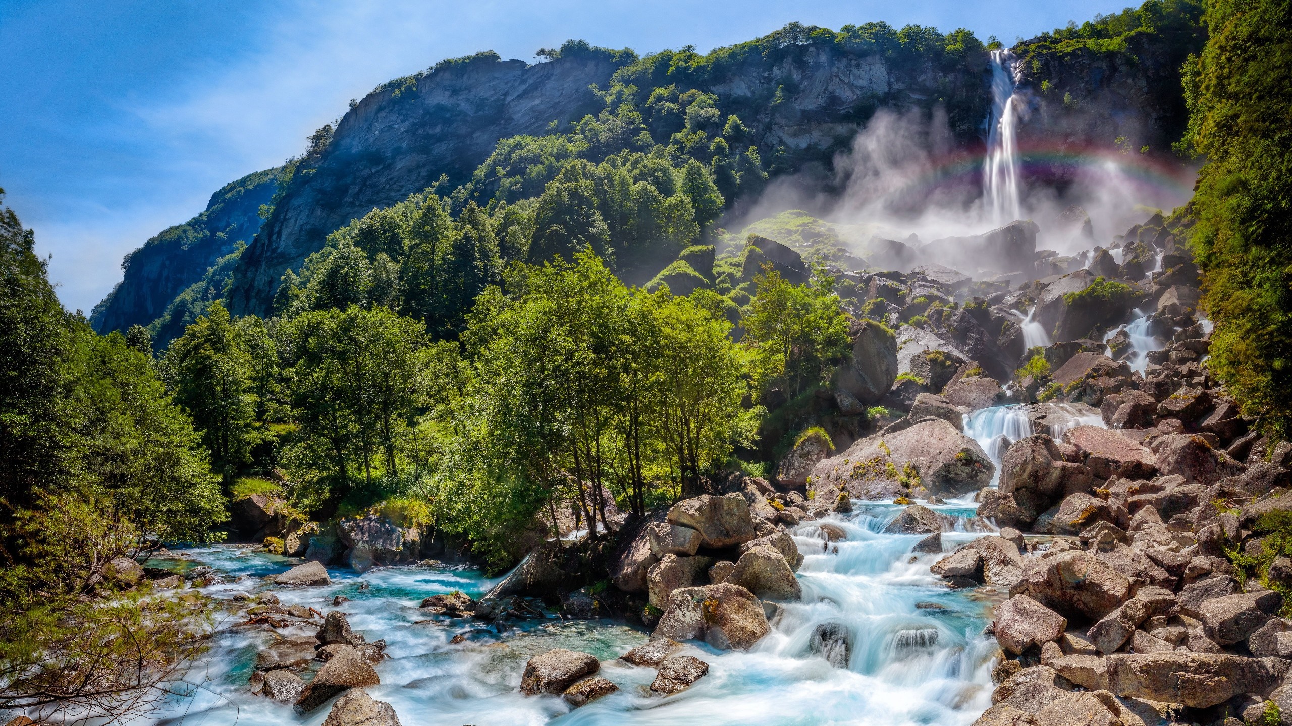 Waterfall cascading over rocks into a river in a forest valley HD Wallpaper