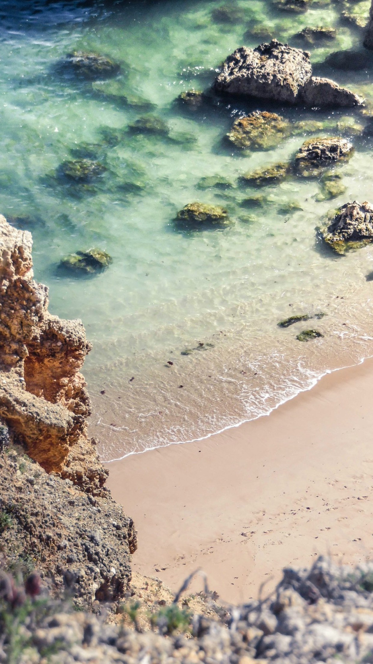 Rocky coast with clear ocean water and sandy beach HD Wallpaper