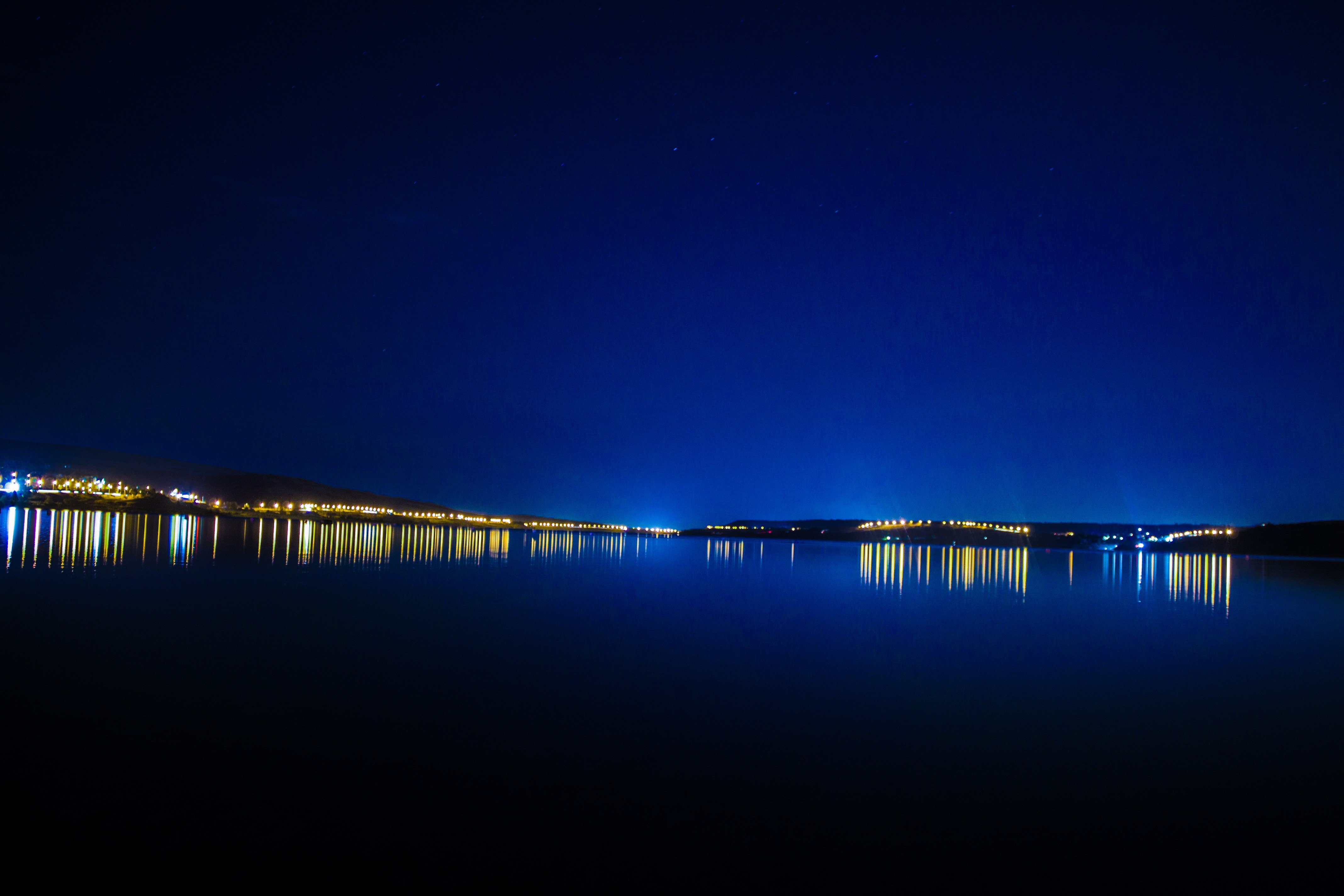 City lights reflecting on a calm lake at night HD Wallpaper